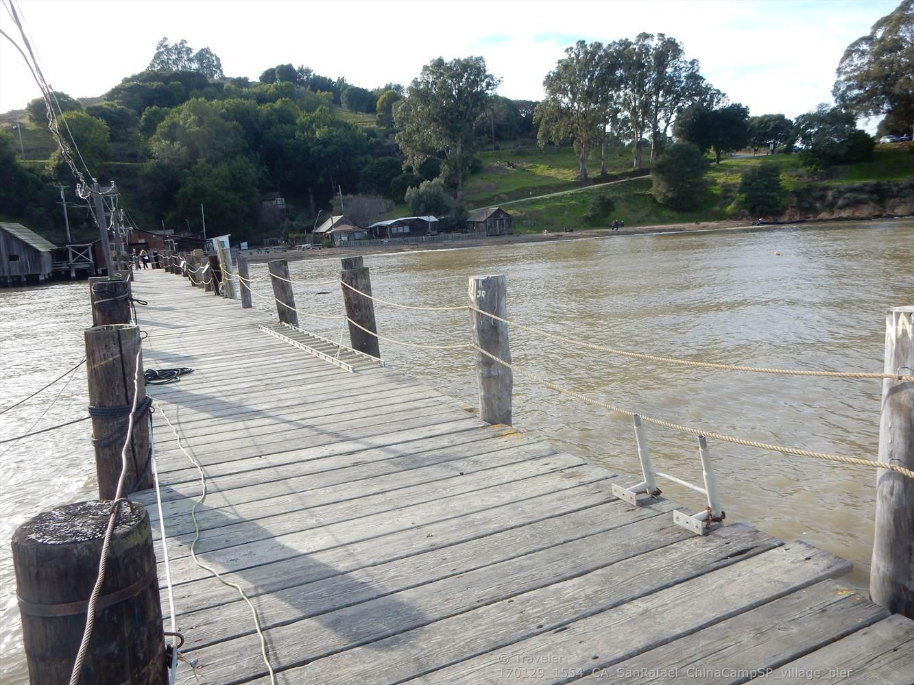 A weathered wooden pier extends over murky water towards distant buildings.