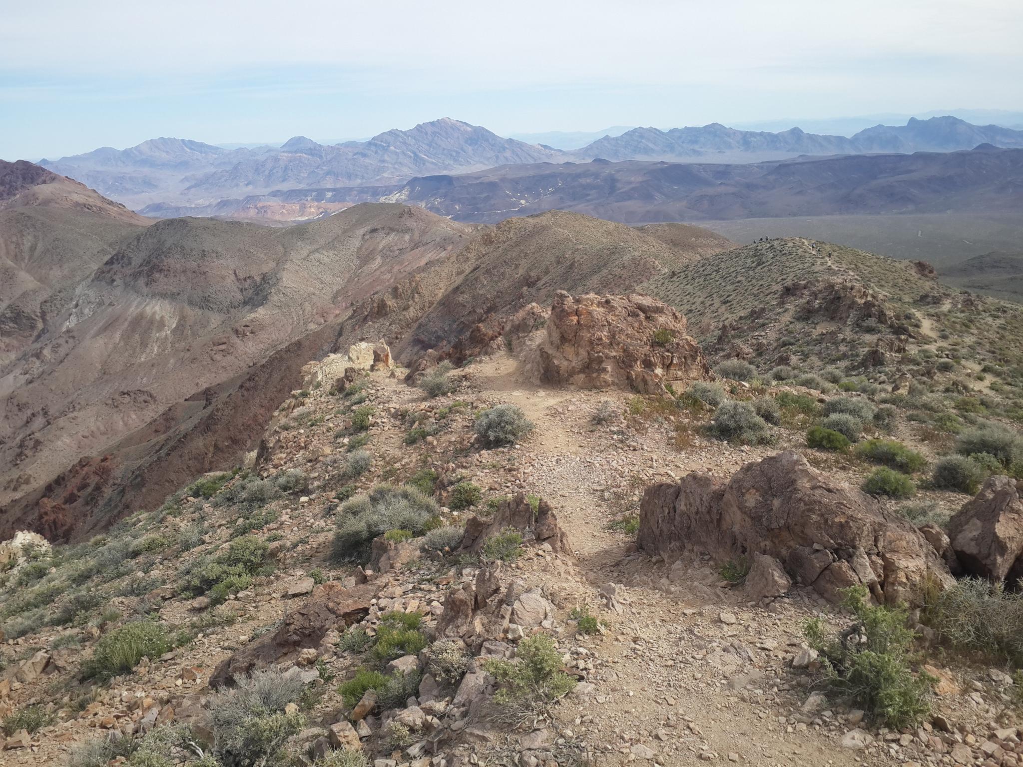 A rocky desert ridge with a winding path and distant mountain ranges.
