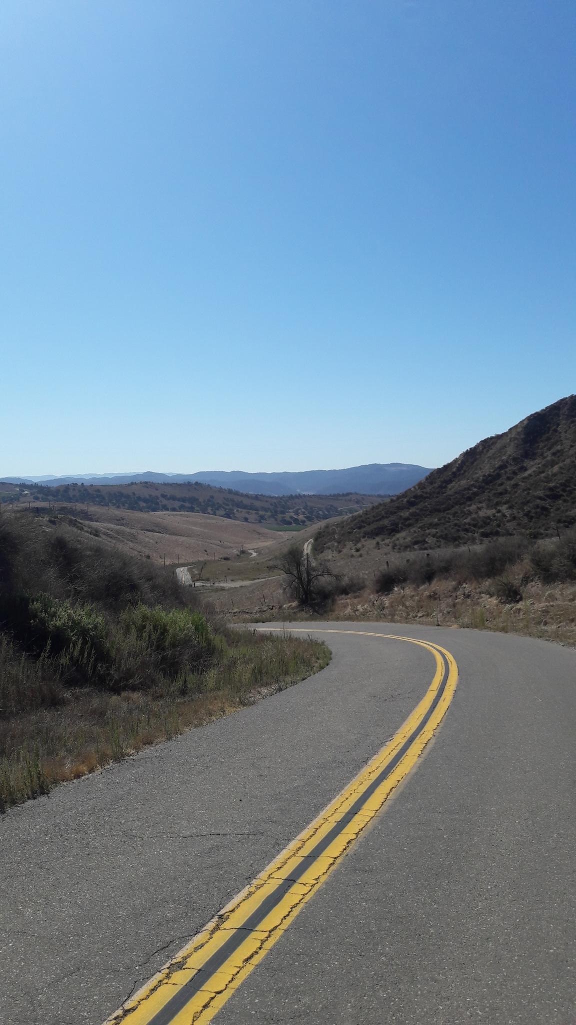 Winding road with double yellow lines through hills under a clear sky.