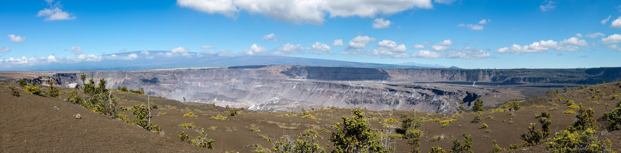A wide panoramic view of a massive, rocky crater under a bright blue sky.