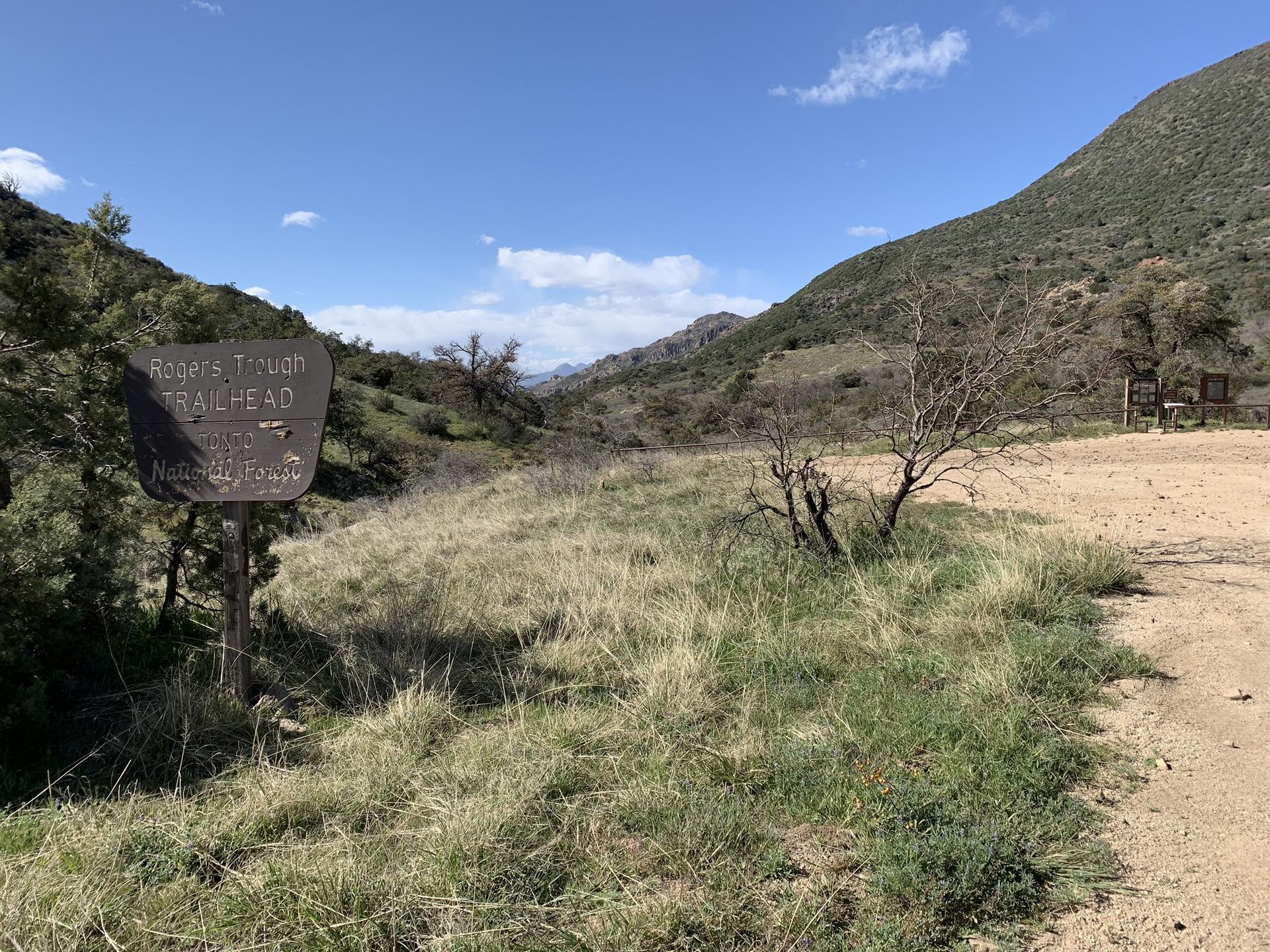 A weathered trailhead sign in a sunny, arid landscape with distant hills.