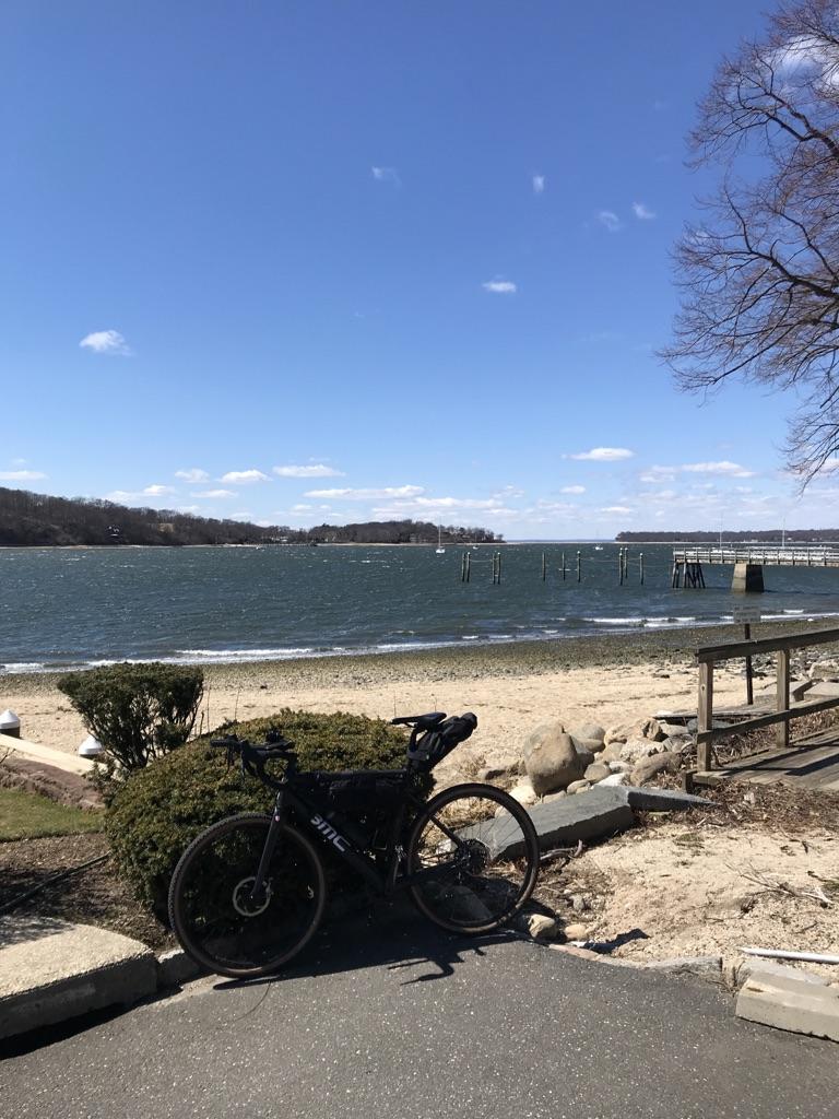 A bicycle parked on a sunny beach next to choppy water.
