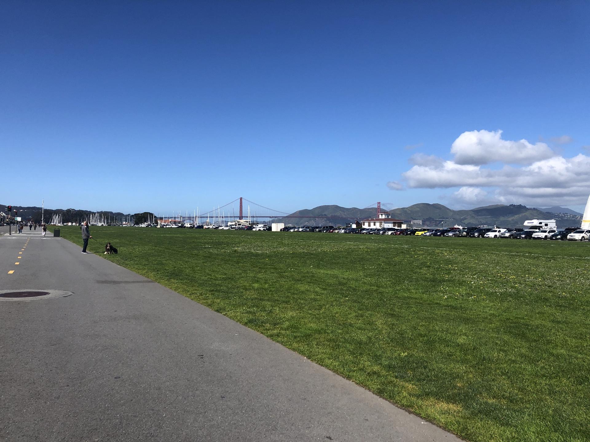 Sunny day over a vast green field with a distant bridge and mountains.