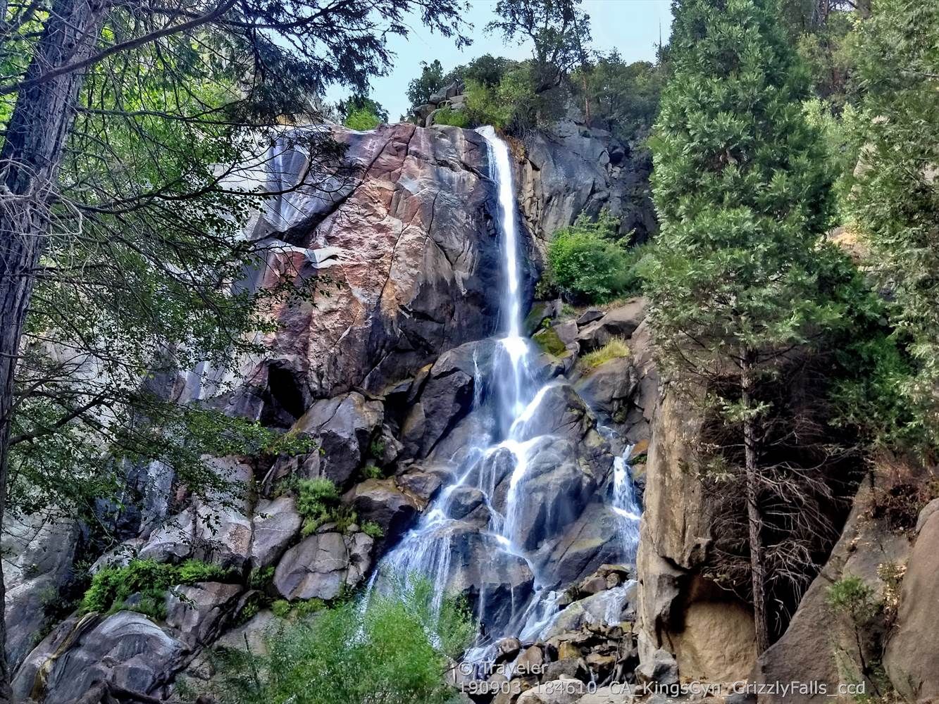 A tall waterfall cascades down a large, rocky cliff surrounded by green trees. - Hume Lake to Kings Canyon National Park via Kings Canyon Scenic Byway