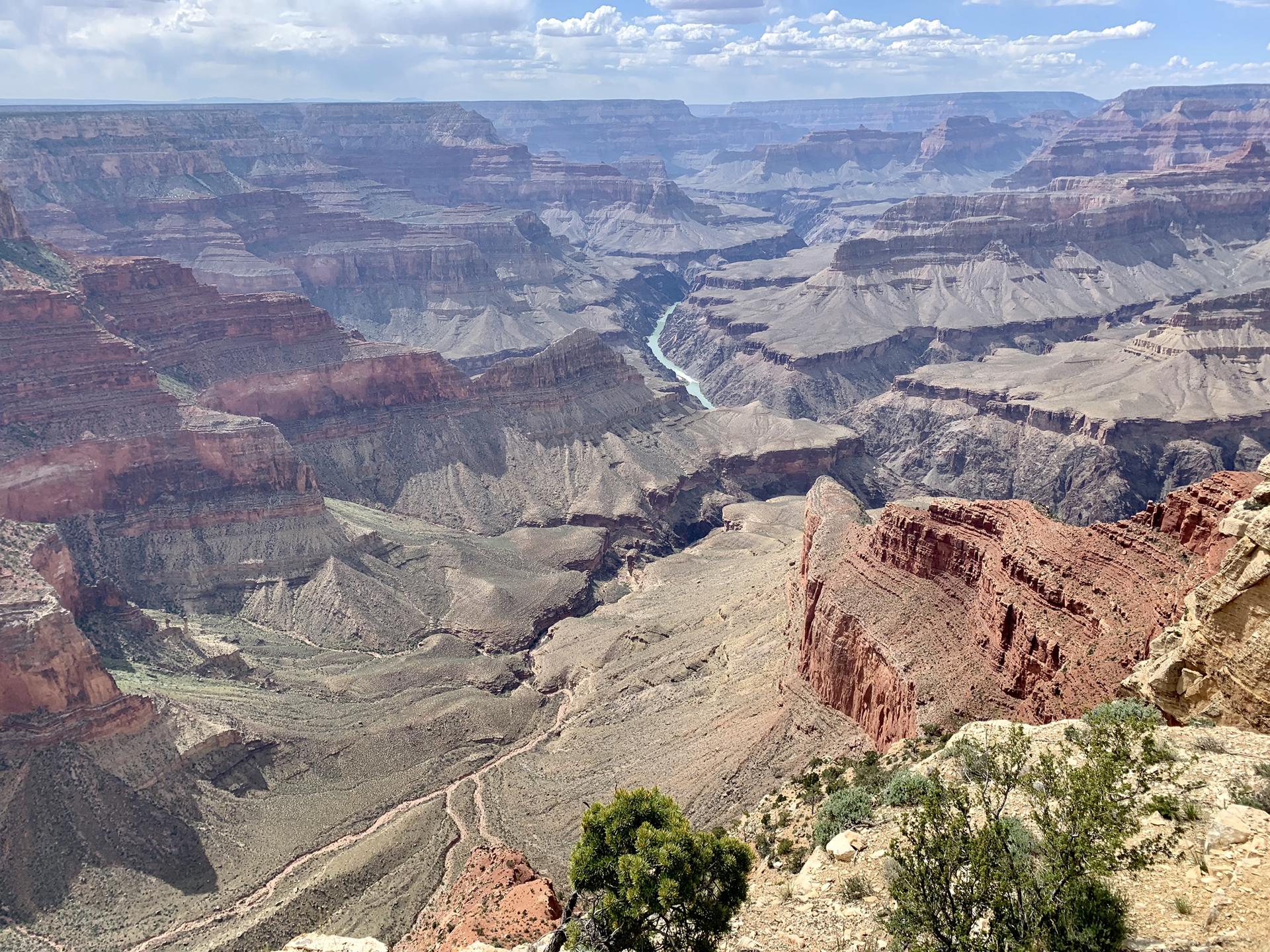 Deep canyon with a winding river and layered rock formations under a cloudy sky.
