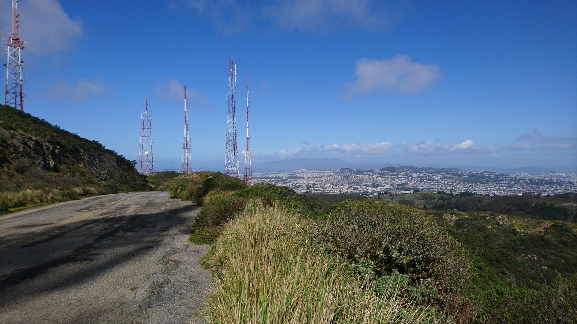 Communication towers on a sunny hillside overlooking a distant city.