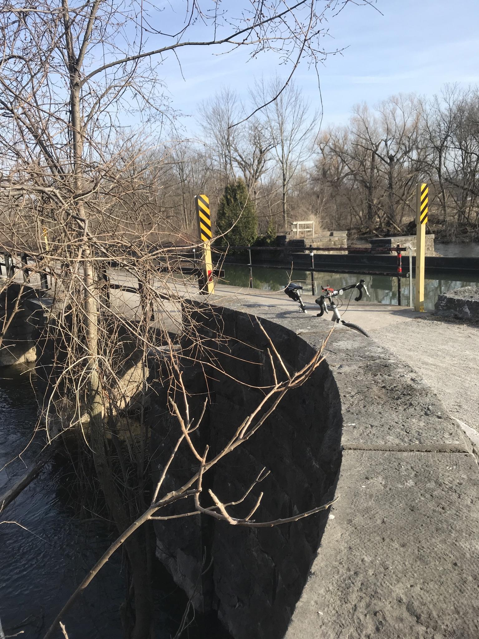 A bicycle parked near a canal lock with bare trees on a clear day.