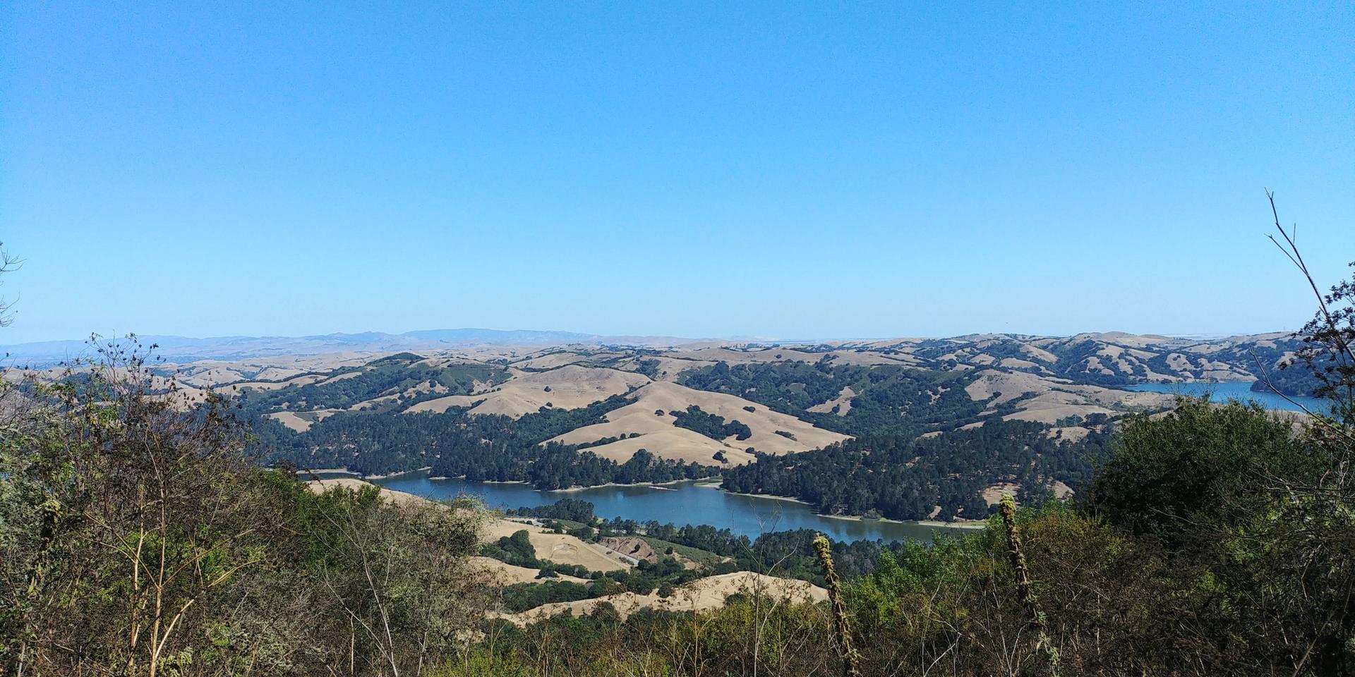 Expansive view of rolling hills, a winding lake, and clear blue sky.