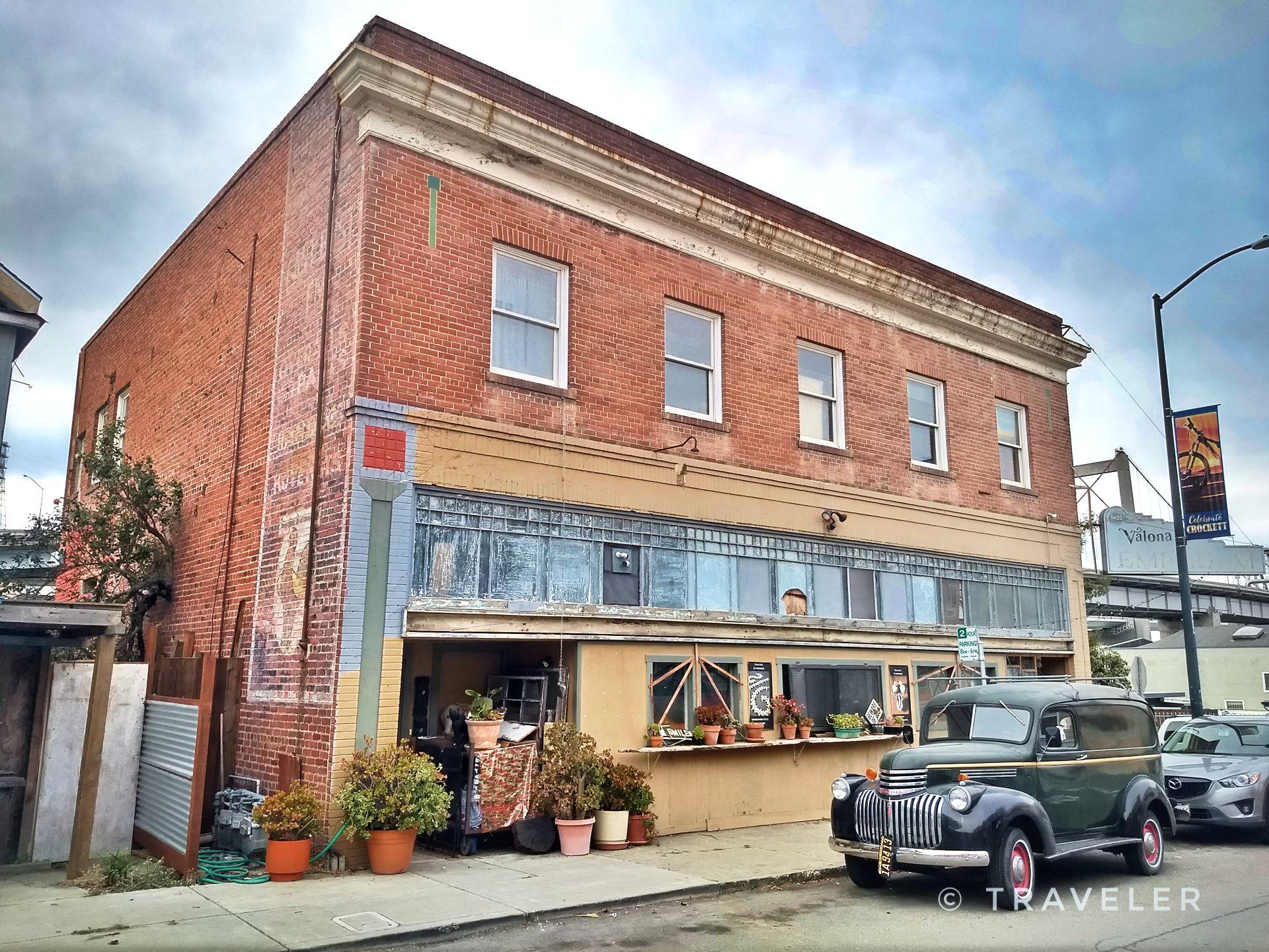 Vintage car parked before an old brick building under a cloudy sky.