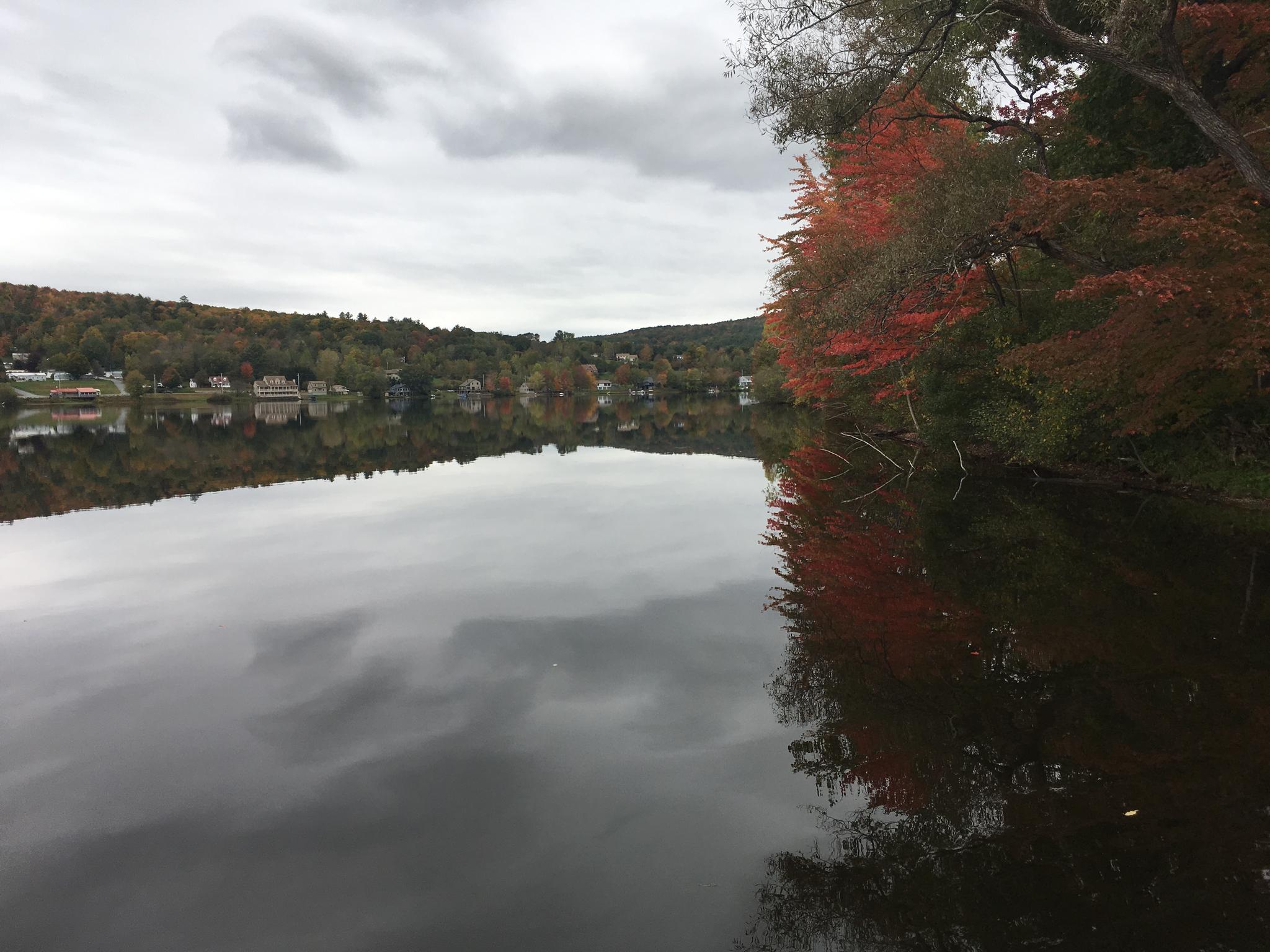 Lake reflecting cloudy sky and vibrant red autumn trees on the shore.