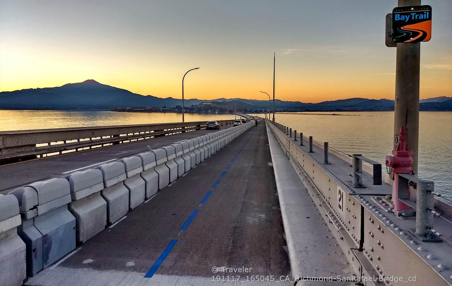 Bridge path over water at sunset with mountains in the distance.