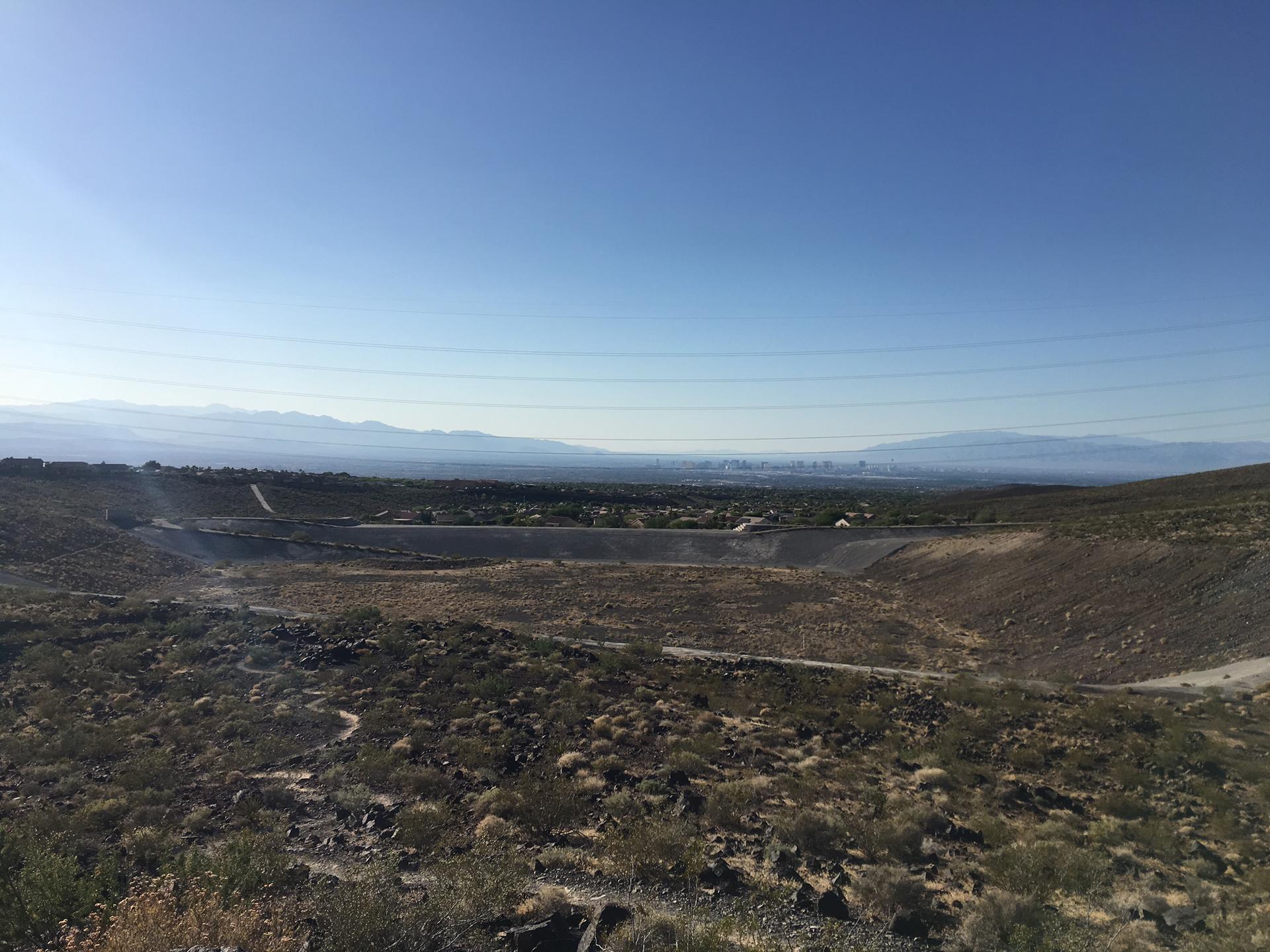 Wide desert landscape with dry brush, distant city, and mountains under clear sky.