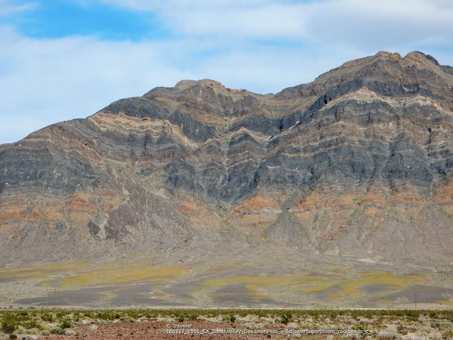 Layered mountain with colorful rock formations under a bright blue sky.