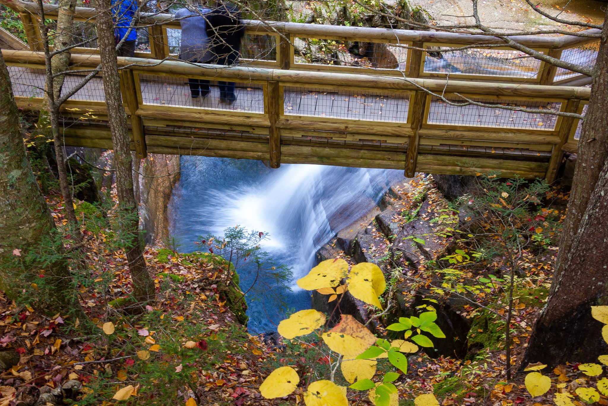 Overhead view of a waterfall under a wooden bridge with people looking down. - Pine Bend Brook Trail to Sabbaday Brook Trail Loop