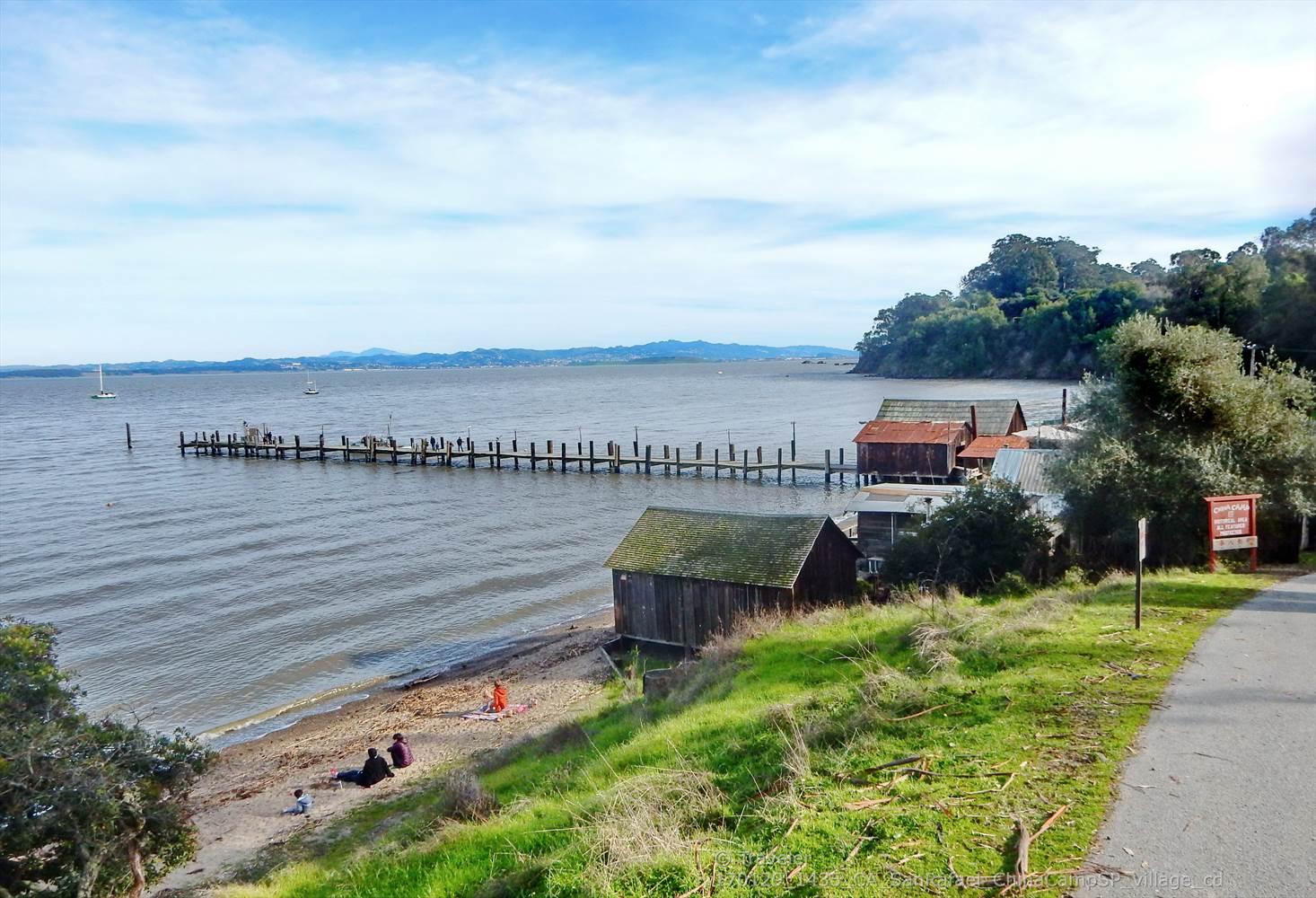 Coastal scene with a long pier, old buildings, and people on the beach.