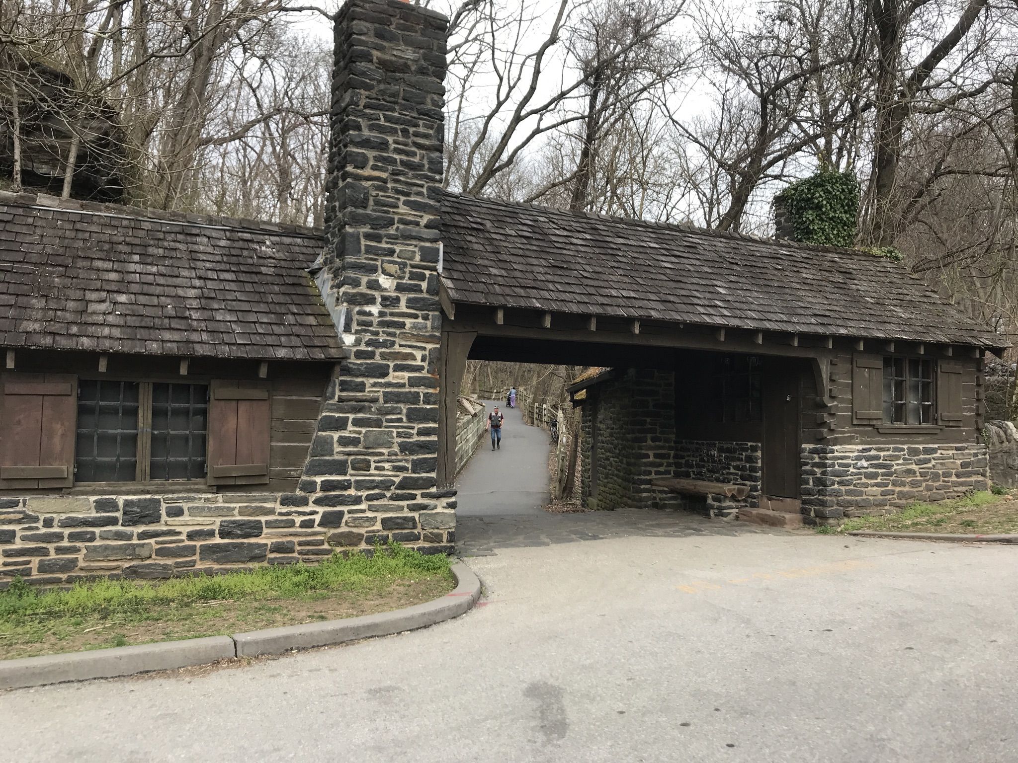 Stone building with covered archway, person walking, bare trees, overcast. - Wissahickon Orange, White, and Yellow Trail Loop