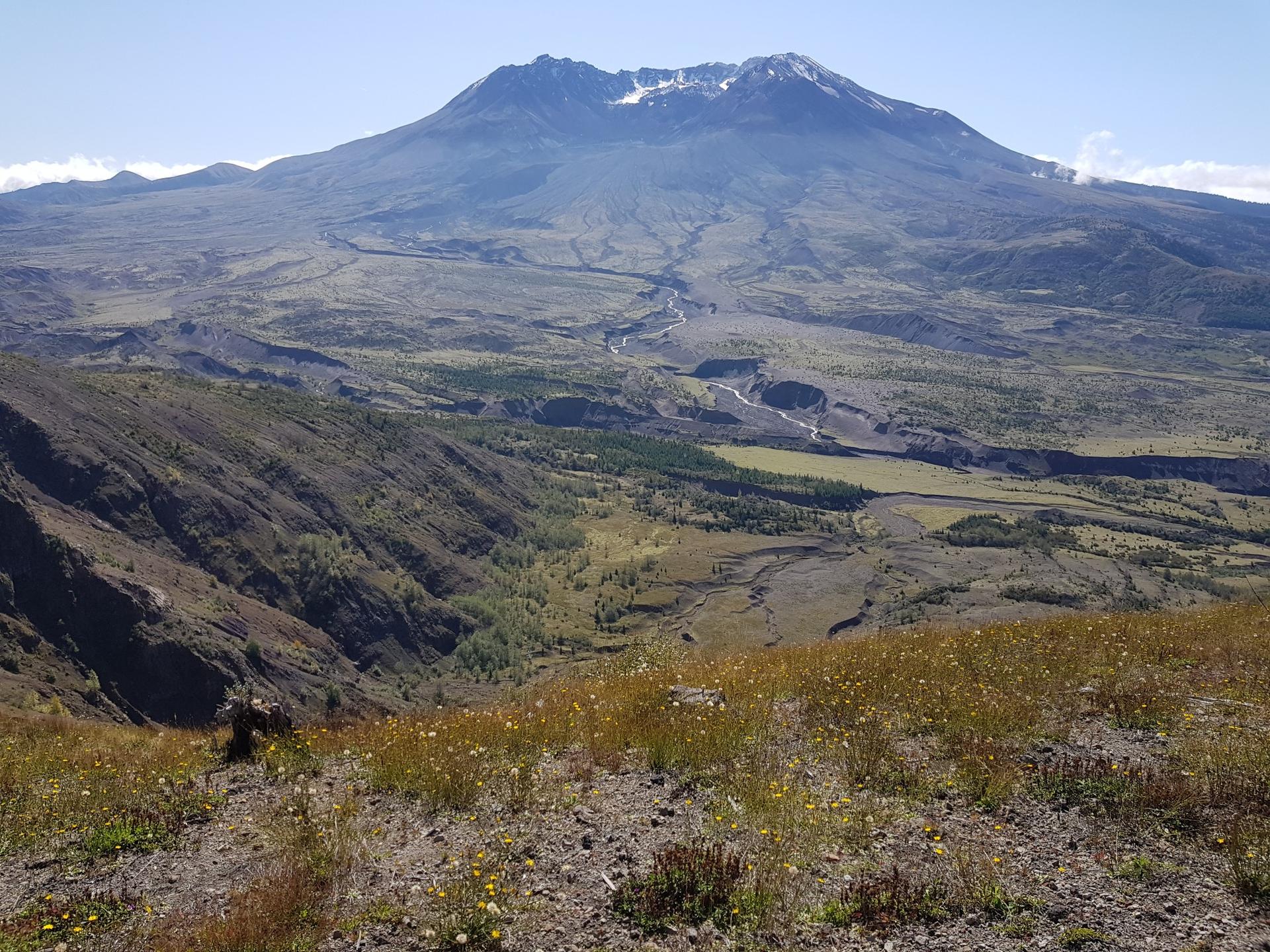 Sunny view of a snow-capped mountain above a vast, rugged valley.