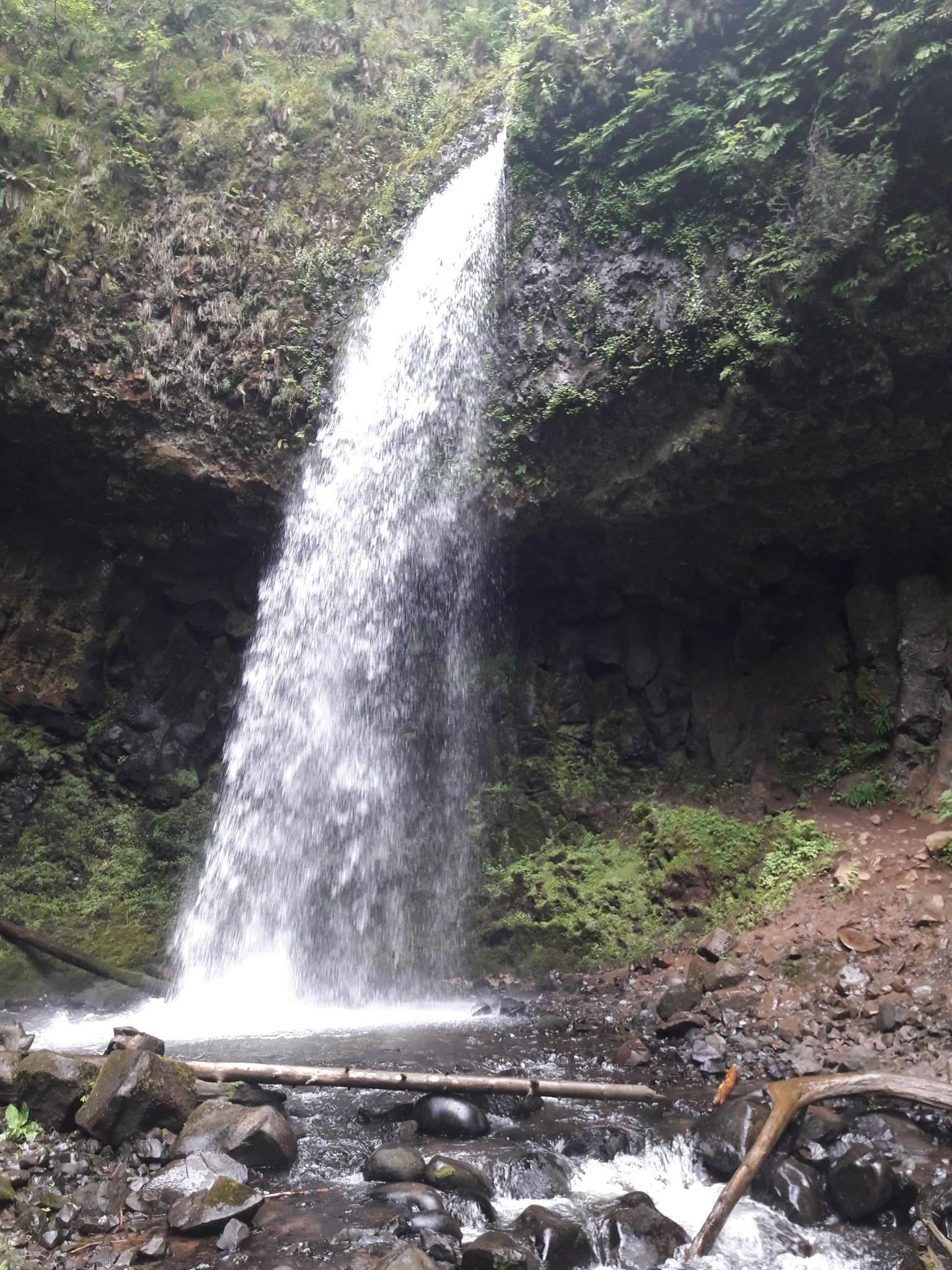 Wide waterfall cascades over a rocky overhang into a stream.