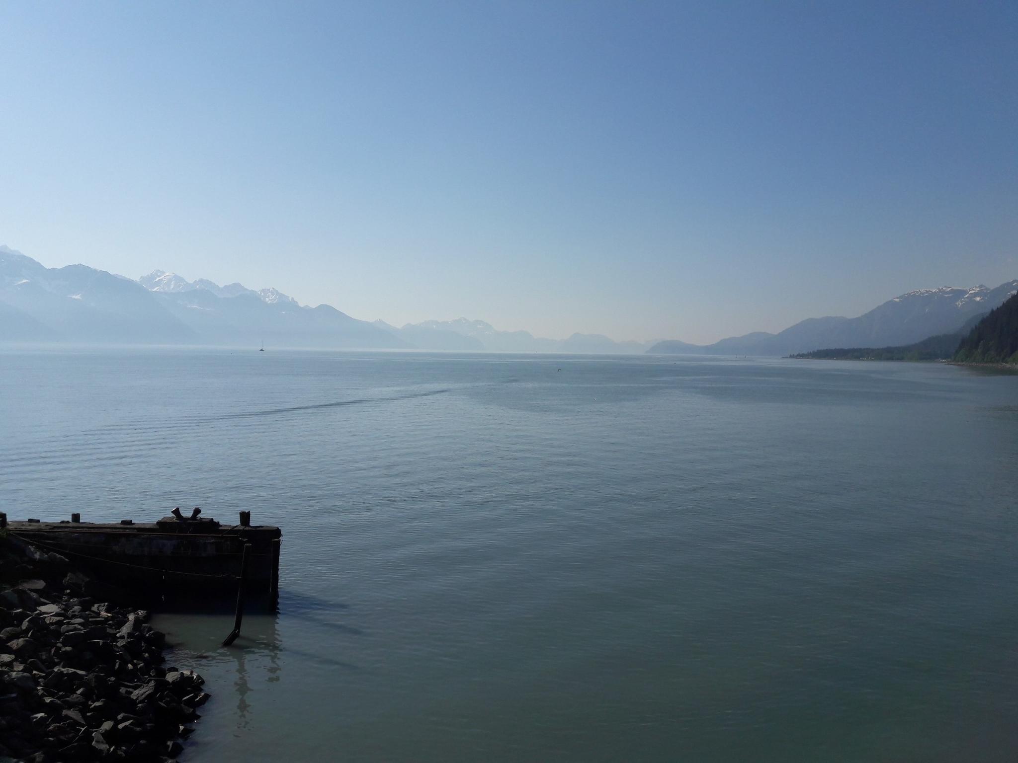 Expansive calm water with distant hazy mountains under a clear blue sky.