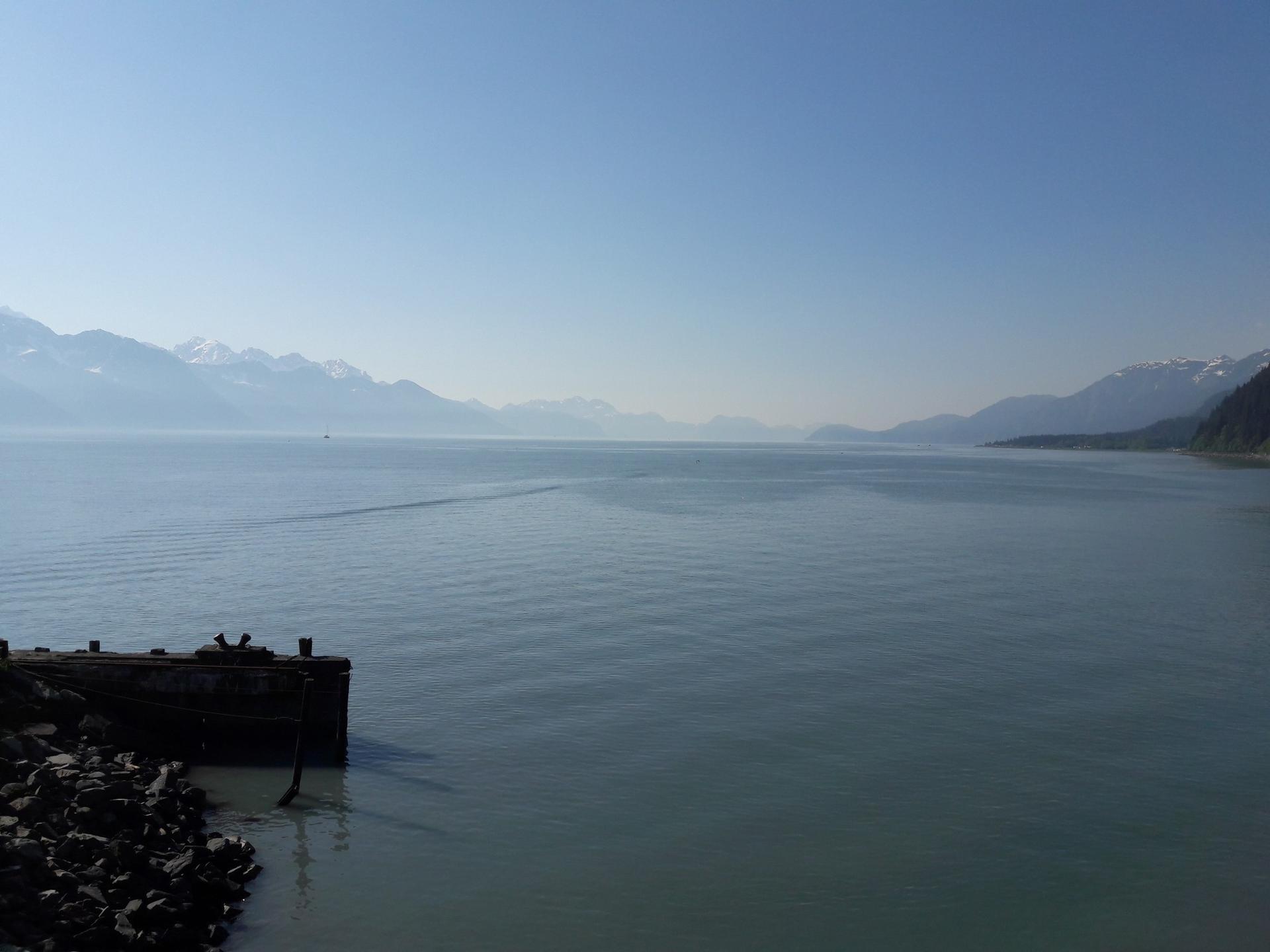 Expansive calm water with distant hazy mountains under a clear blue sky.