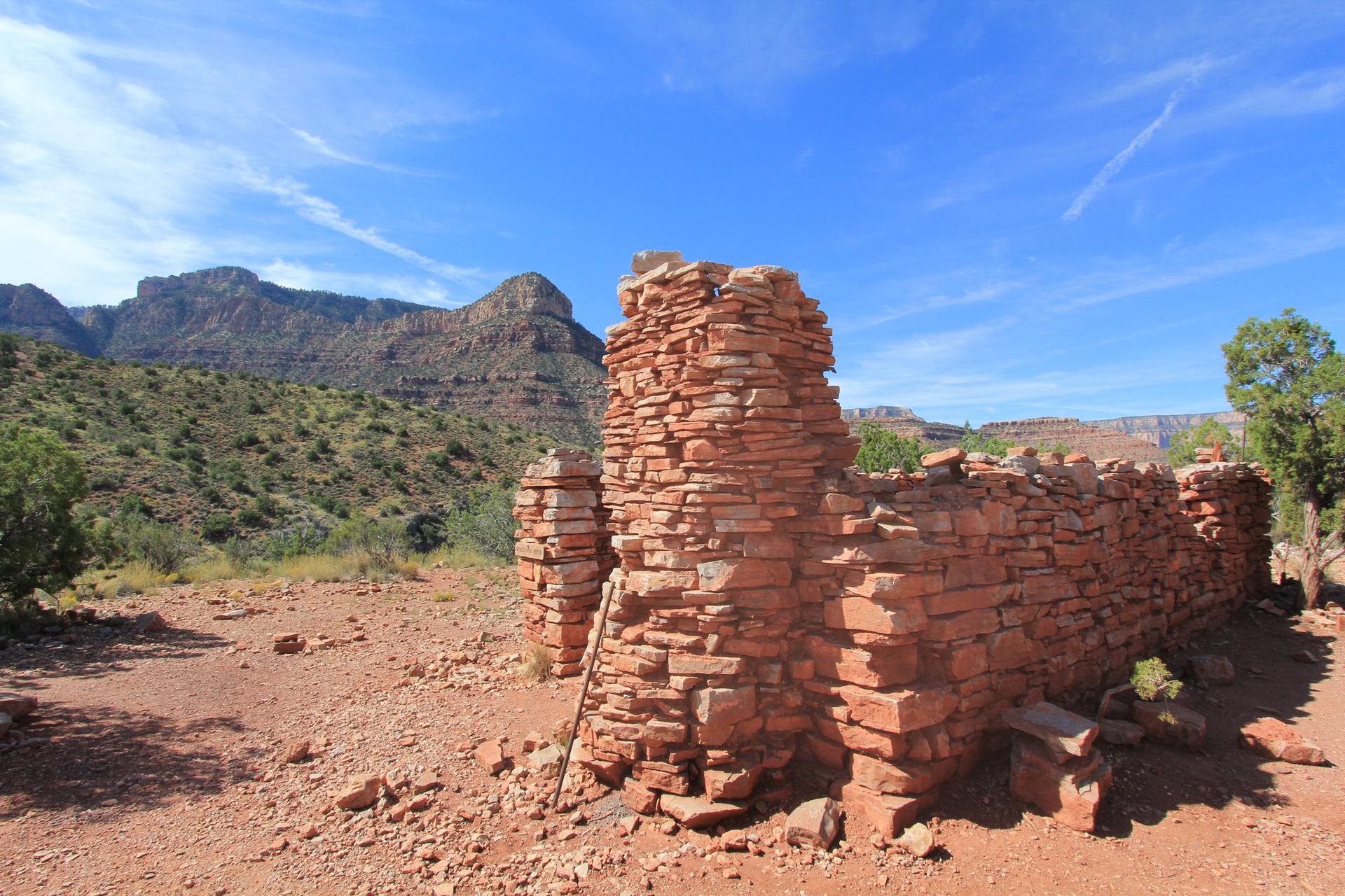 Sunny view of ancient red stone ruins in a desert valley with mountains.