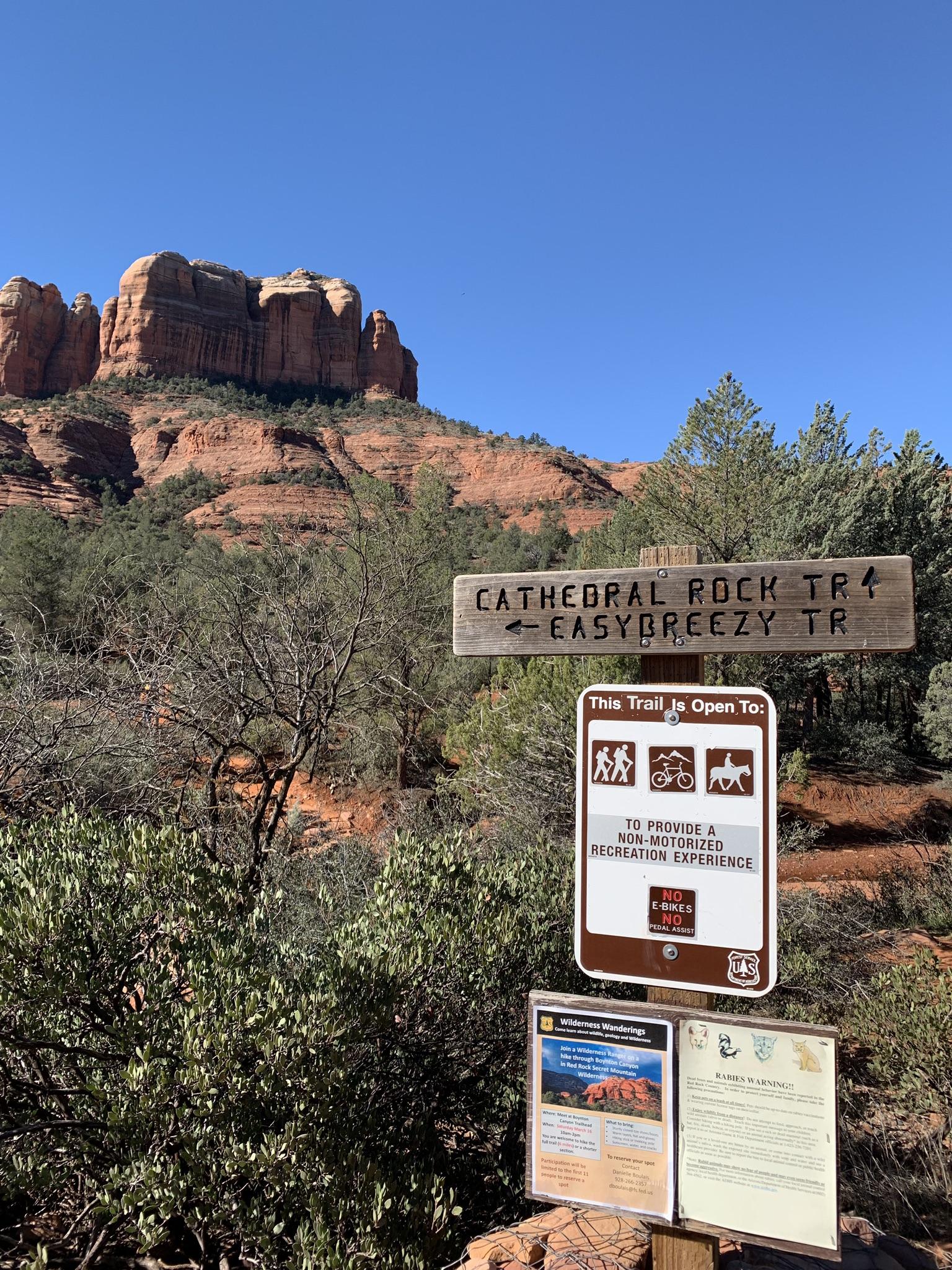 Trail sign and information boards with a large red rock formation behind.