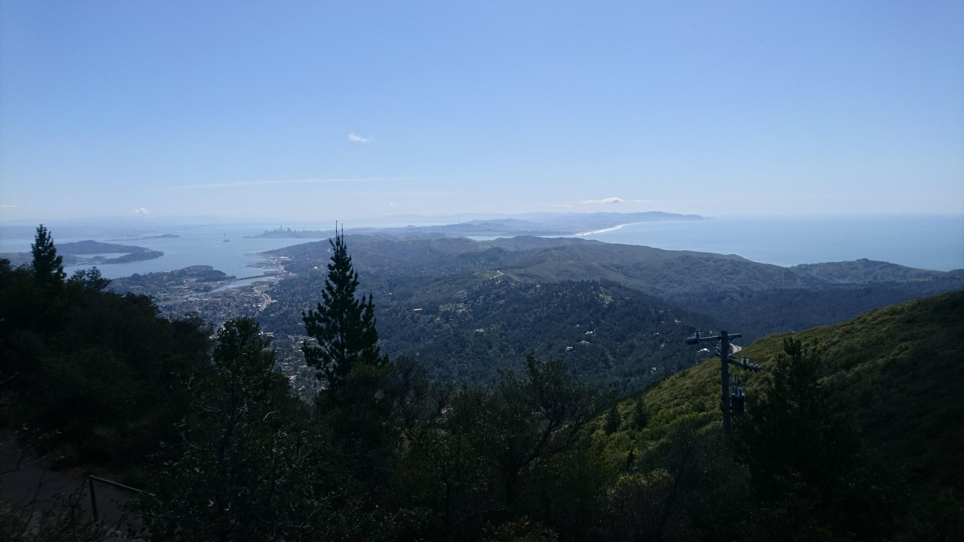 Panoramic view of a bay, distant ocean, and forested hills on a clear day.