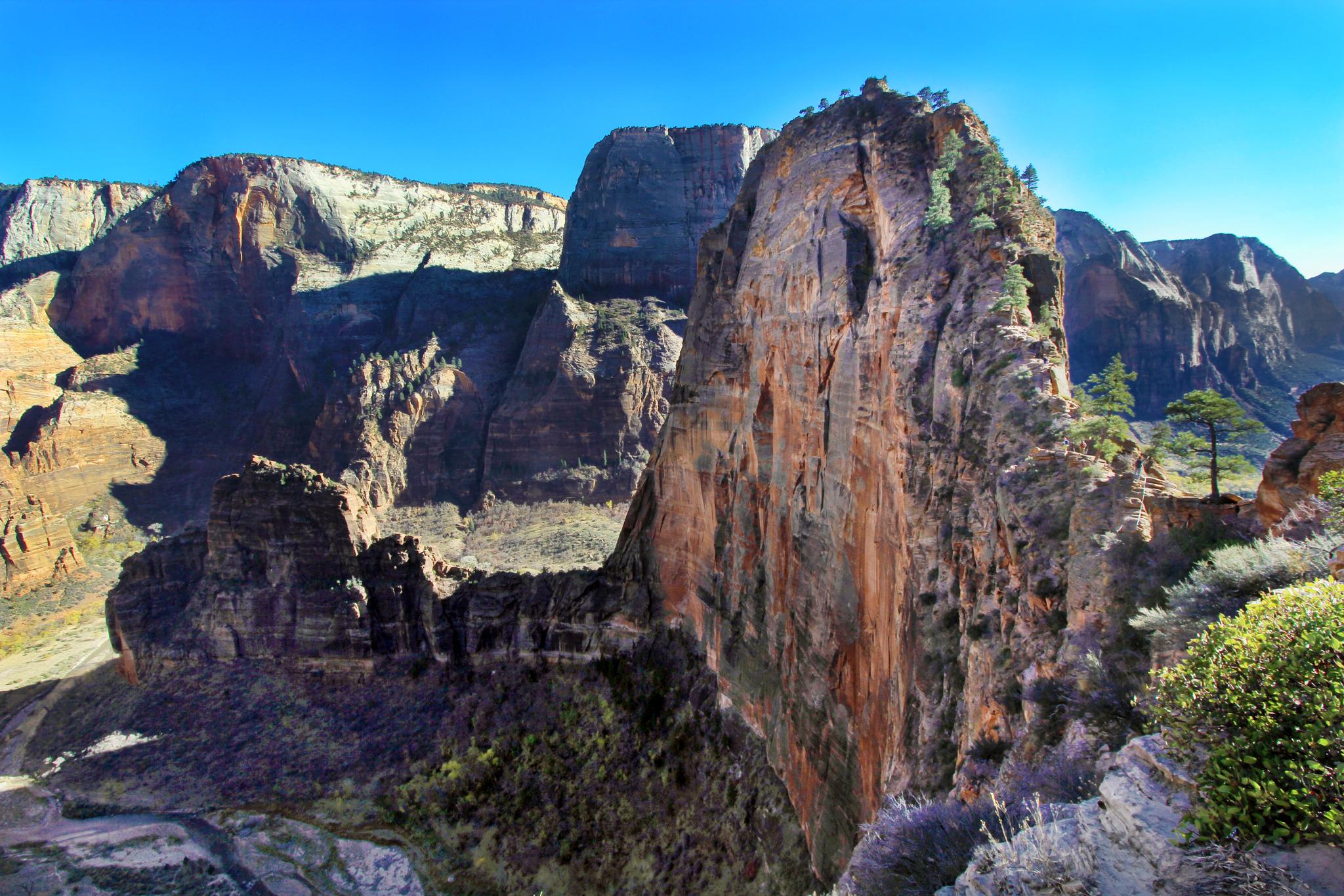 Towering, colorful rock formations dominate a deep canyon under a clear blue sky.