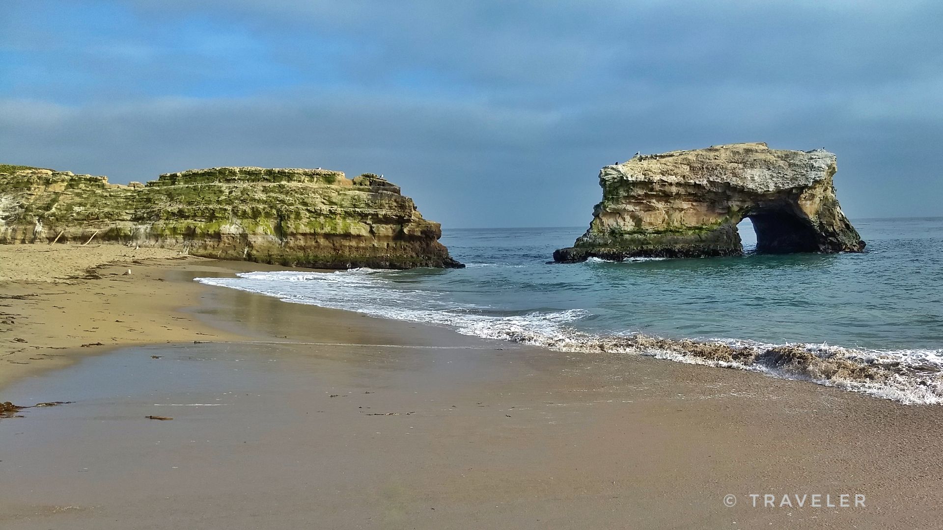 Sandy beach with ocean waves and two large rock formations, one arched. - Moore Creek Trail