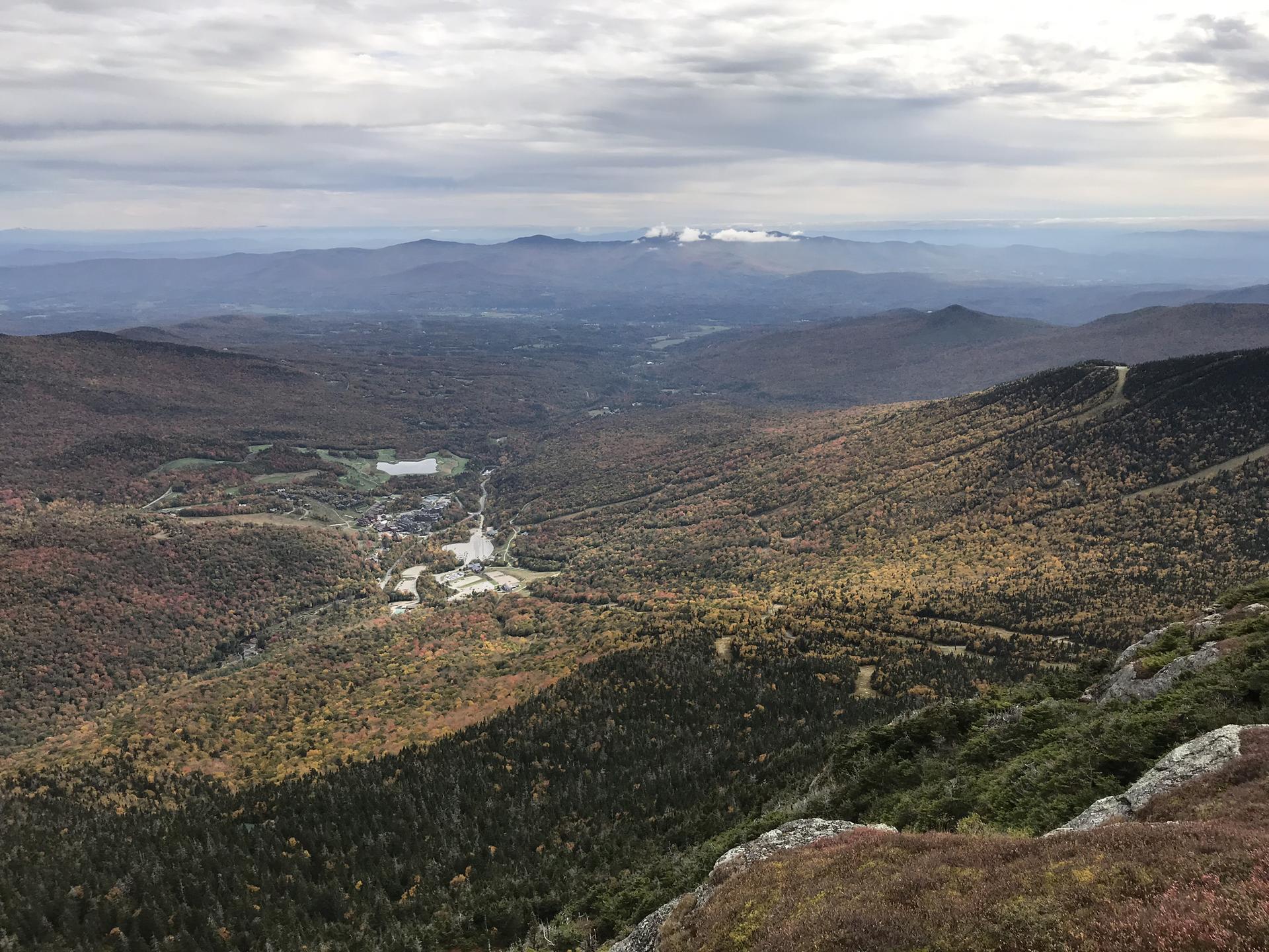 Overcast view of an autumn valley with distant mountains and a small town.
