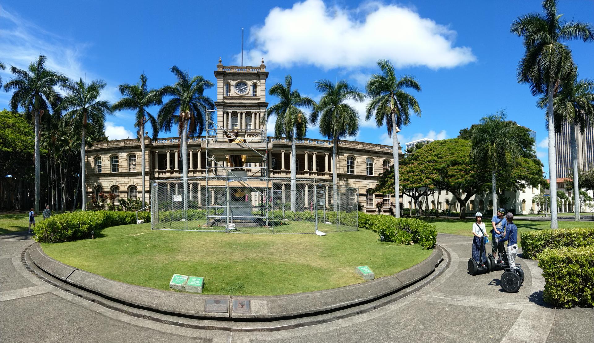 Historic building with clock tower, palm trees, and people on Segways.