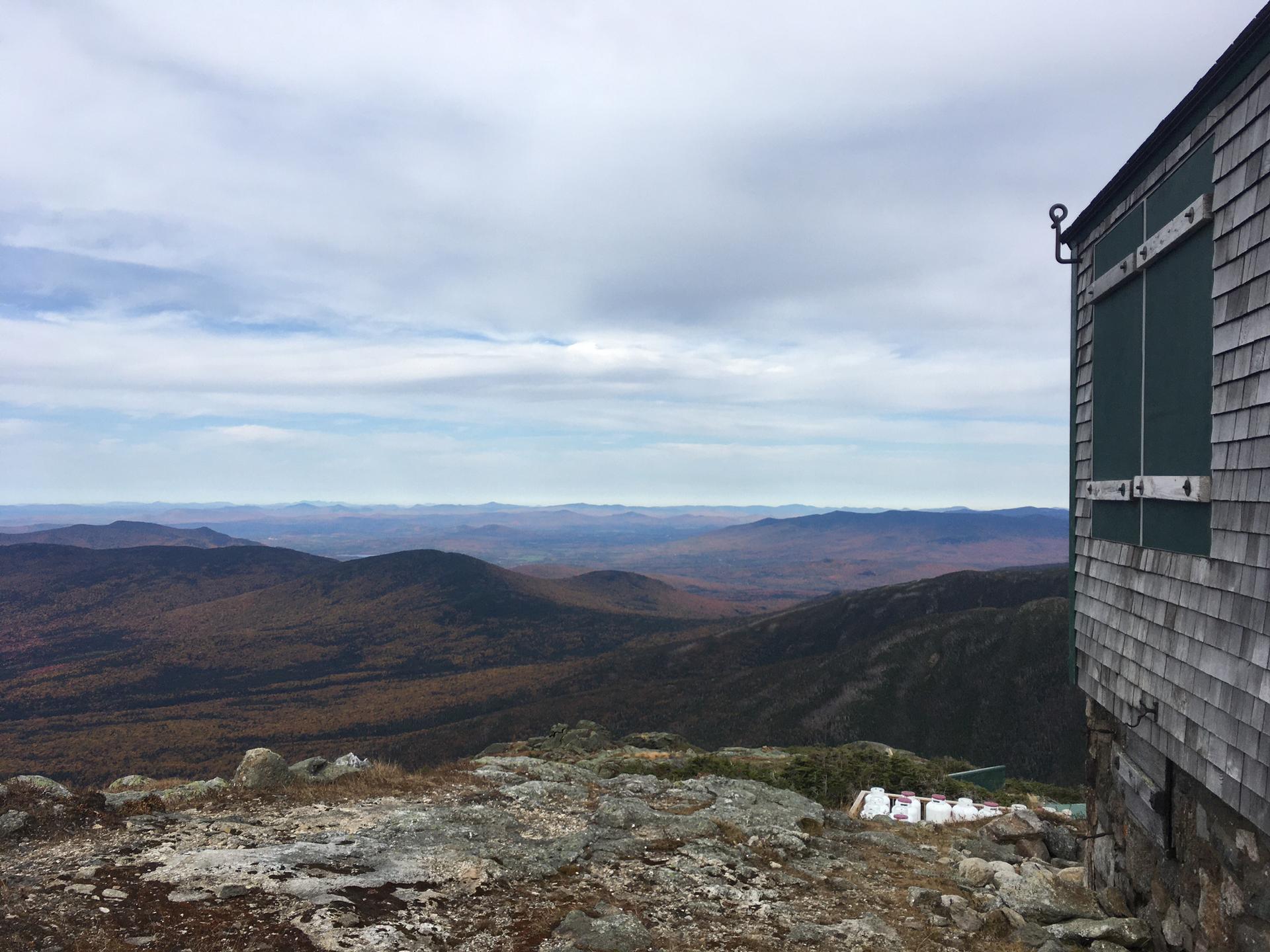 A weathered building overlooks a vast mountain landscape under a cloudy sky.