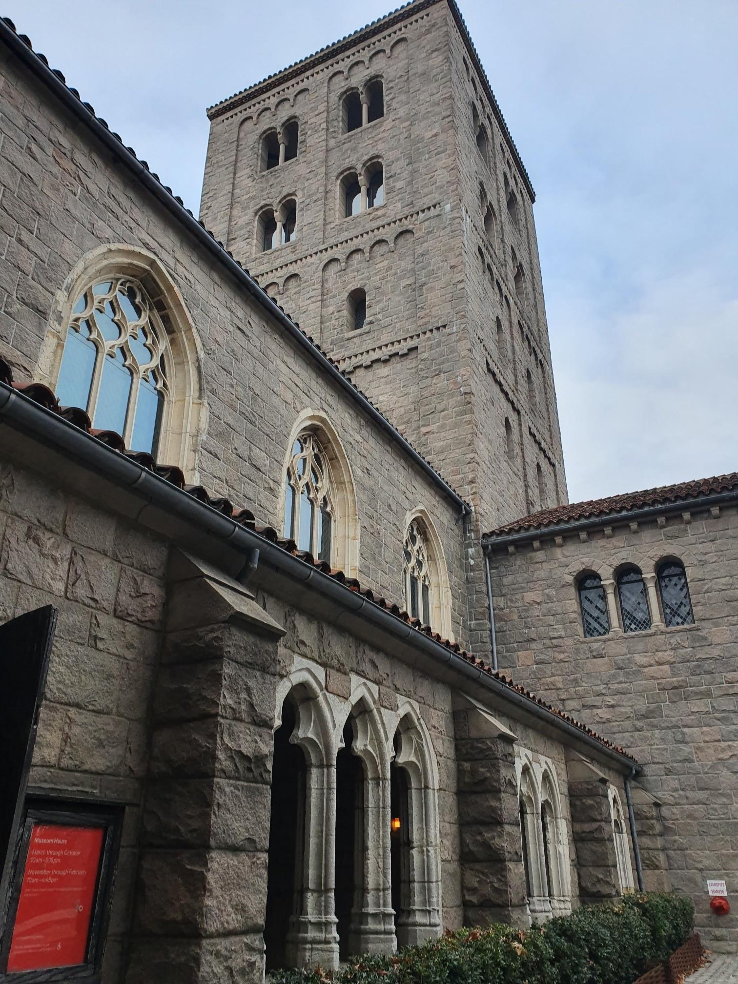 Tall stone building with a tower and arched windows under a cloudy sky.