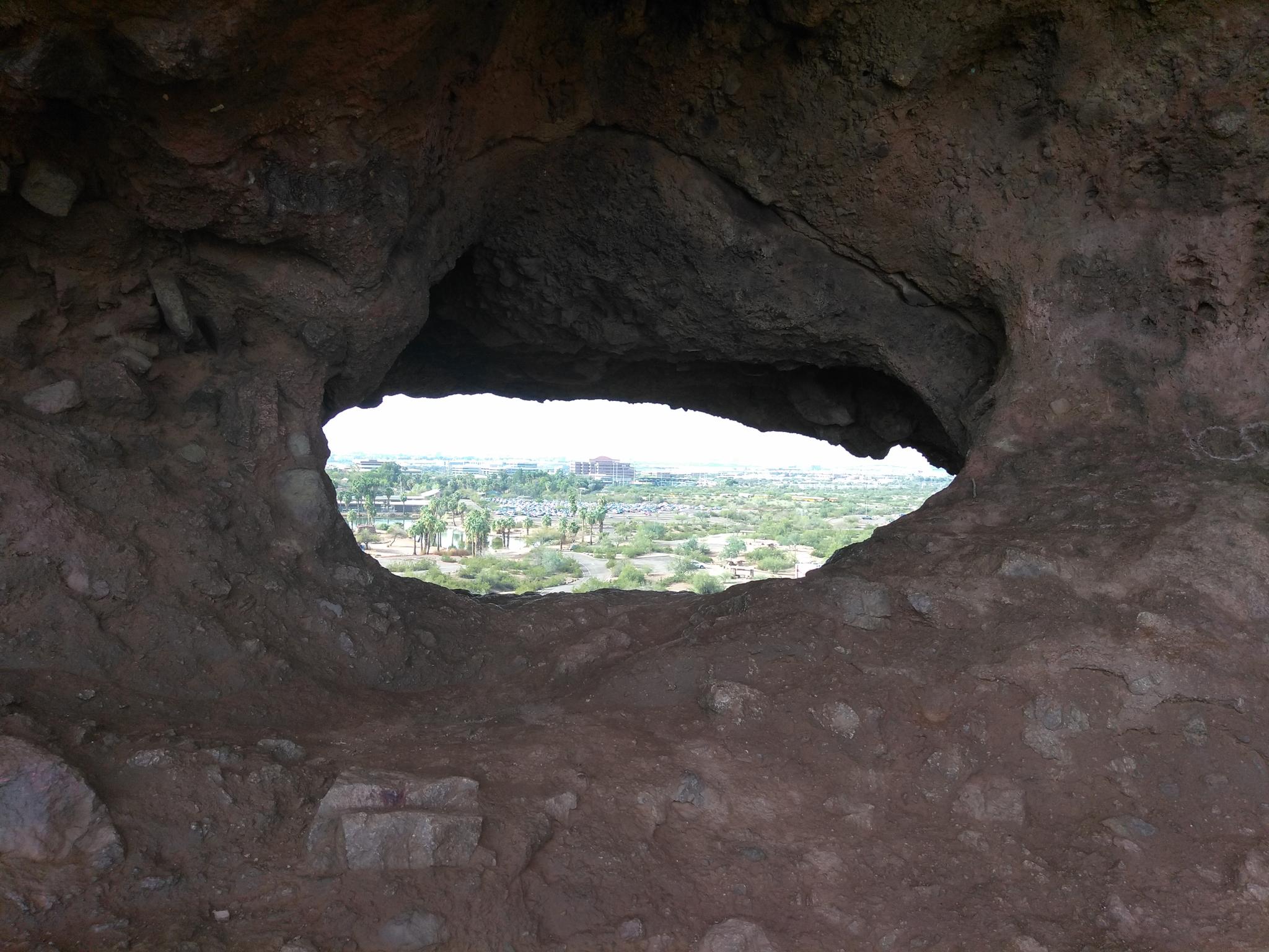 View of a distant landscape through a dark, natural rock cave opening.