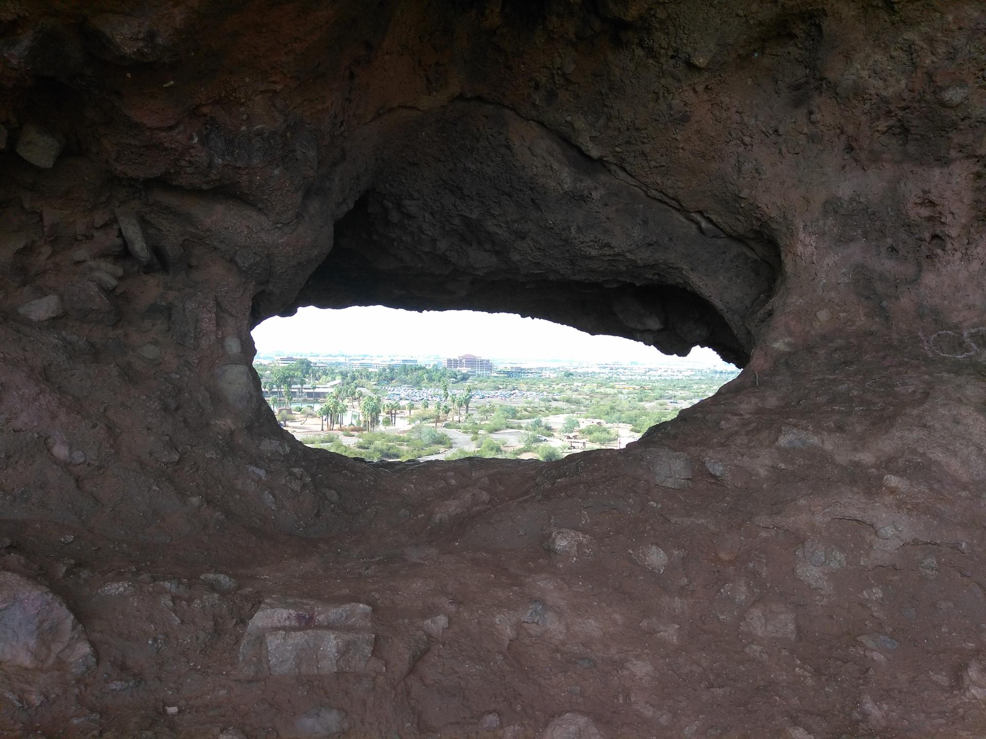 View of a distant landscape through a dark, natural rock cave opening.