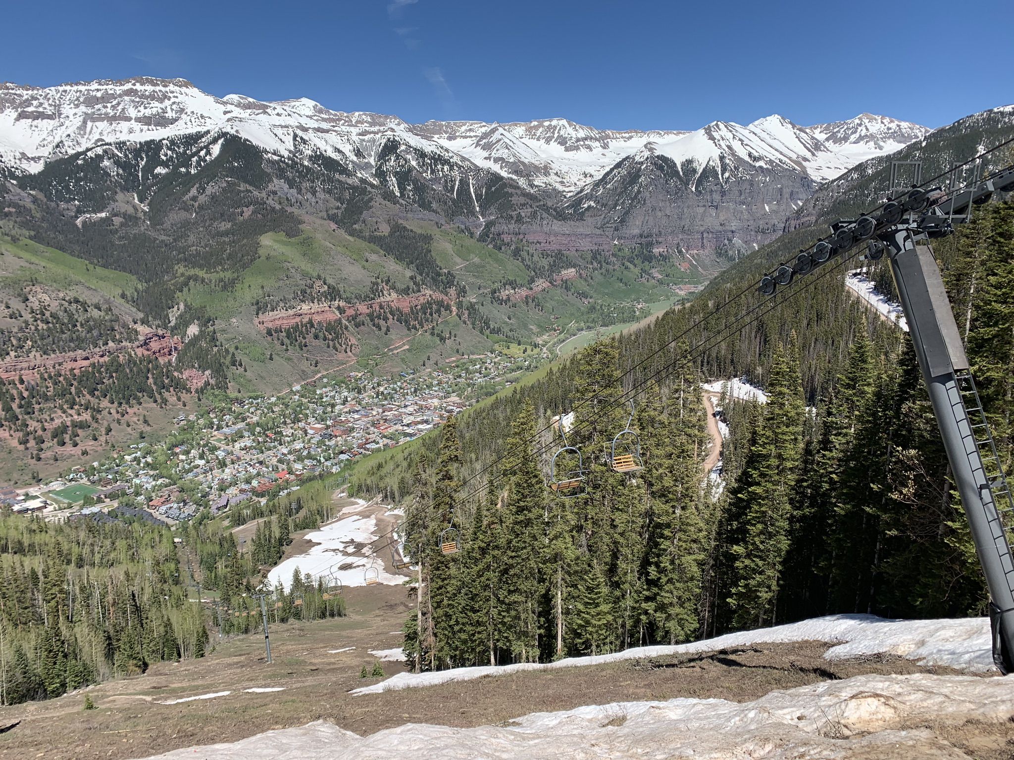 Sunny mountain valley with town, pine trees, snow, and ski lift. - See Forever Trail