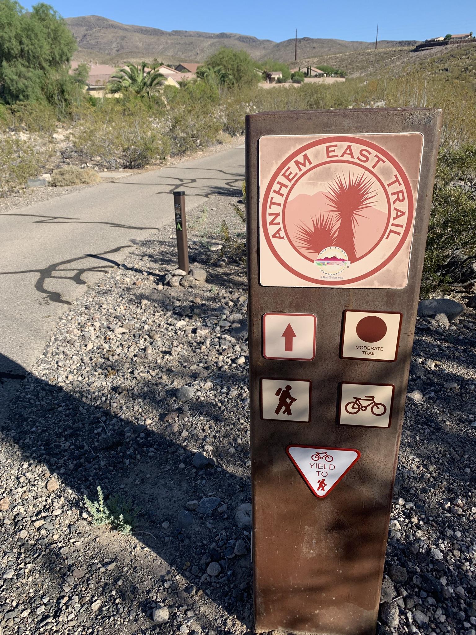 A trail sign with symbols for hiking and biking on a sunny desert path.