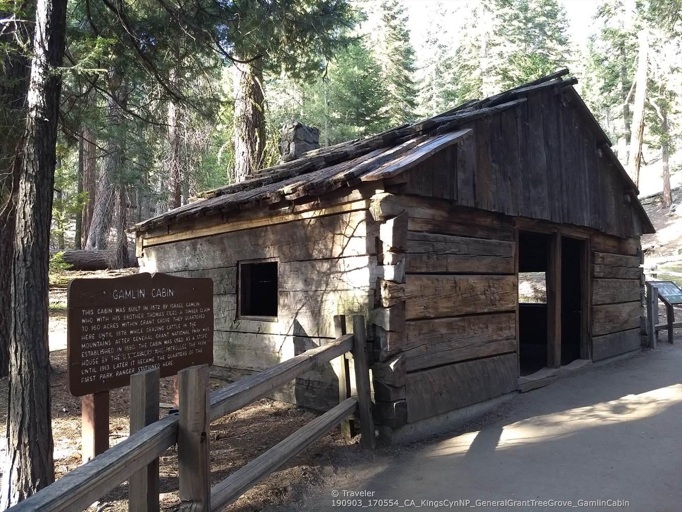 An old wooden log cabin with a fence in a sunlit forest.
