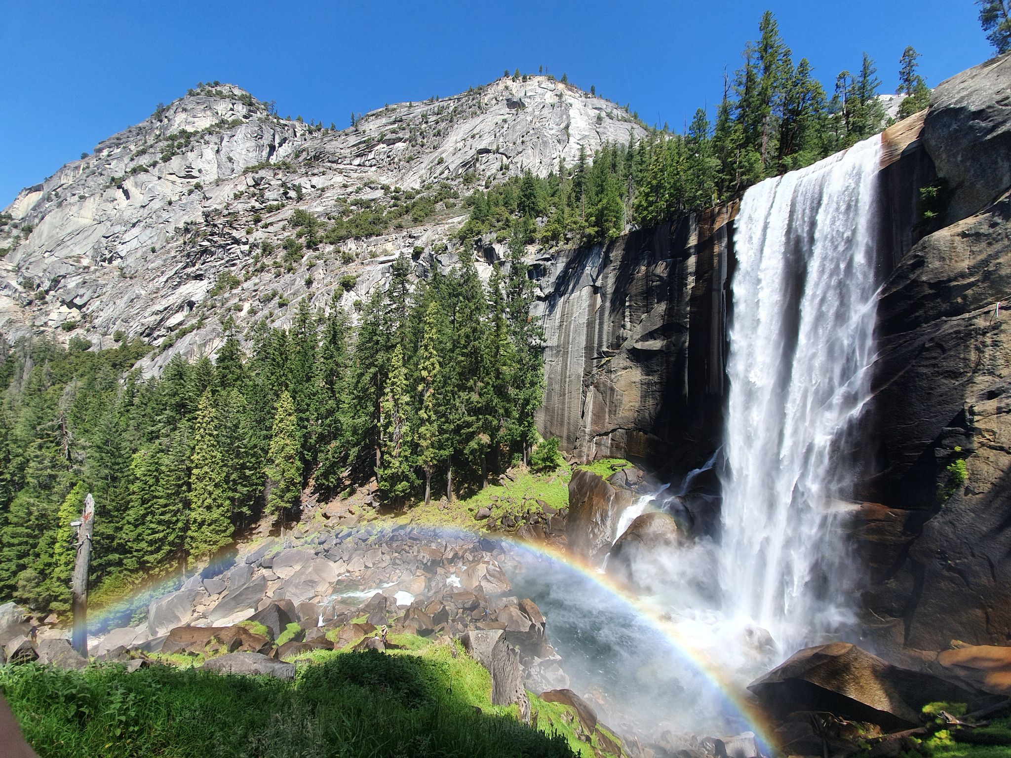 A powerful waterfall plunges down a cliff, creating a rainbow in bright sunlight. - Vernal Fall and Clark Point Loop via Mist Trail and John Muir Trail