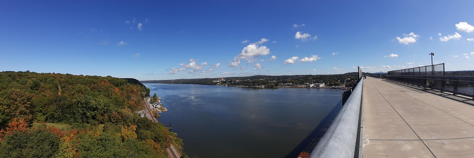 Wide river, autumn trees, and a bridge walkway under a bright blue sky.
