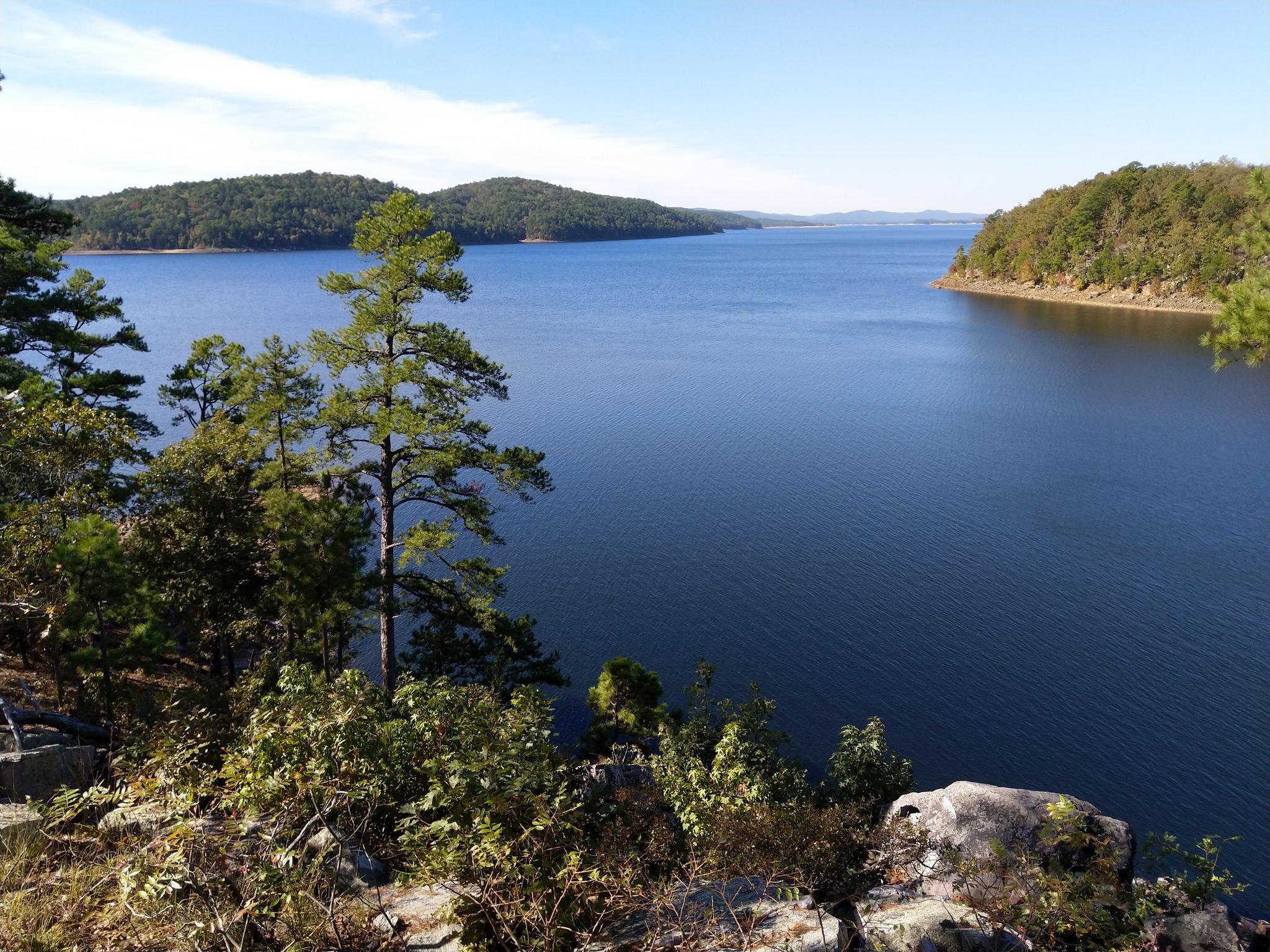 Expansive blue lake surrounded by green forested hills under a clear sky.