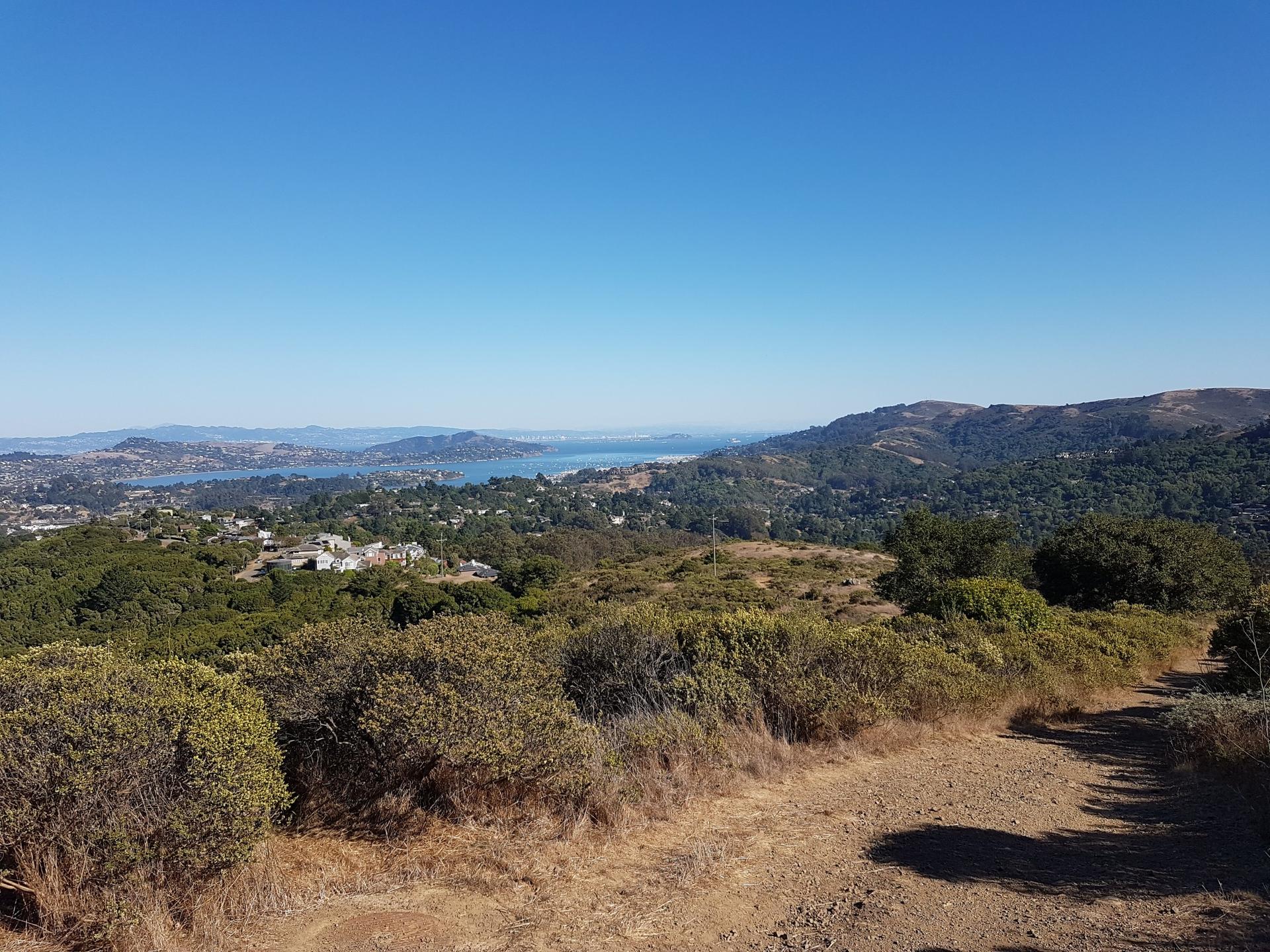 Panoramic view of green and dry hills, distant water under a clear sky.