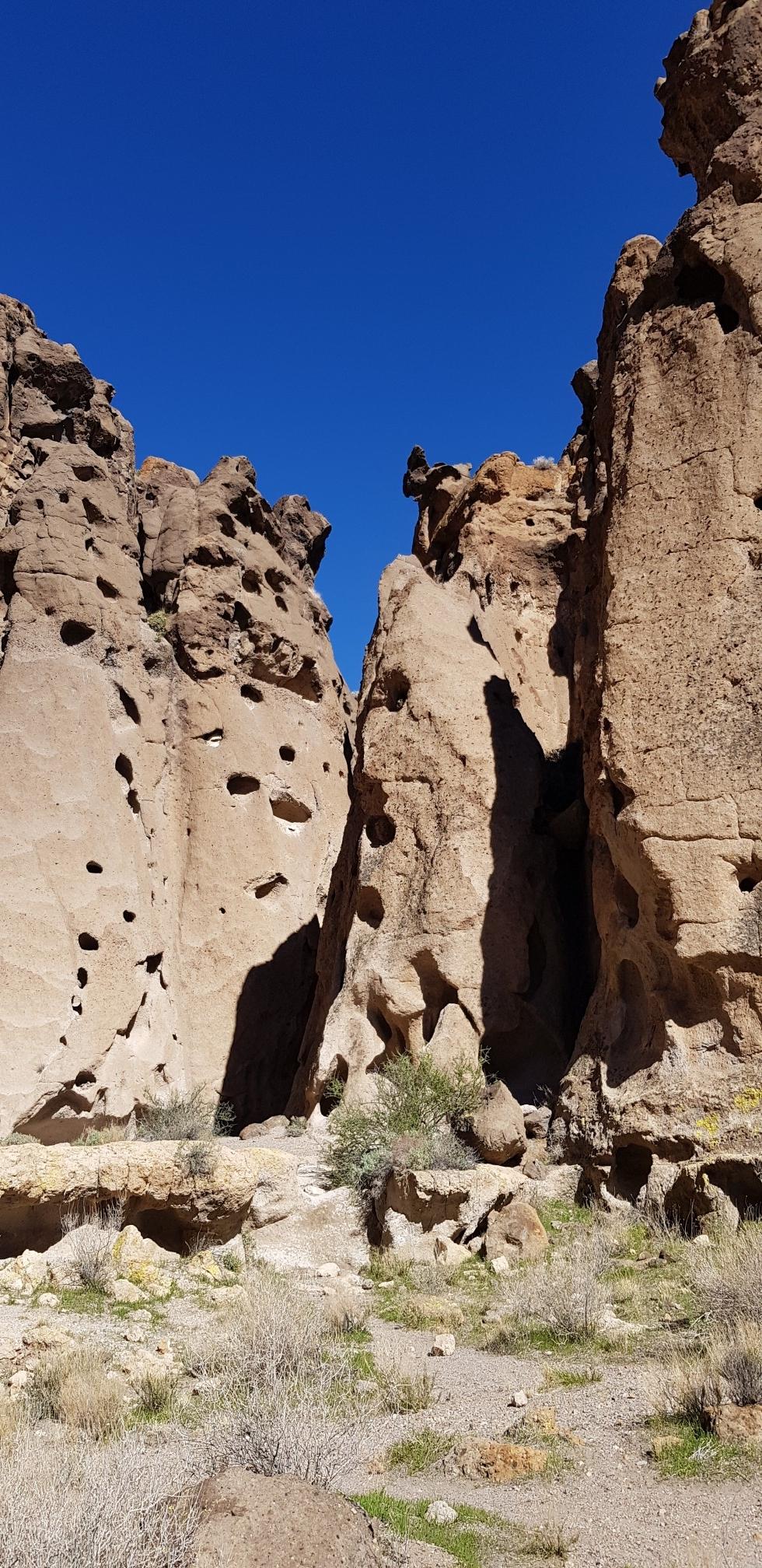 Tall, eroded rock formations with many holes stand under a clear blue sky.