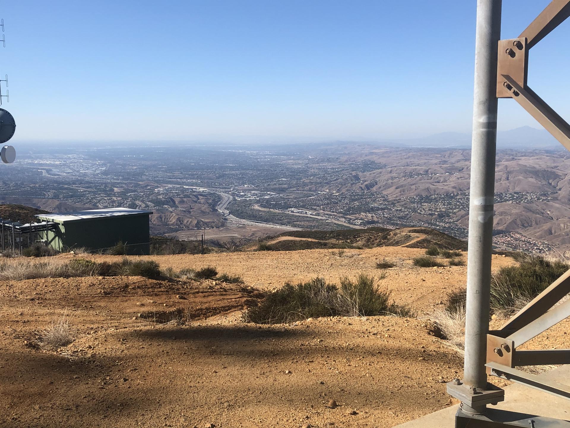 Panoramic view of a distant city and valley from a dry, sunny hilltop.