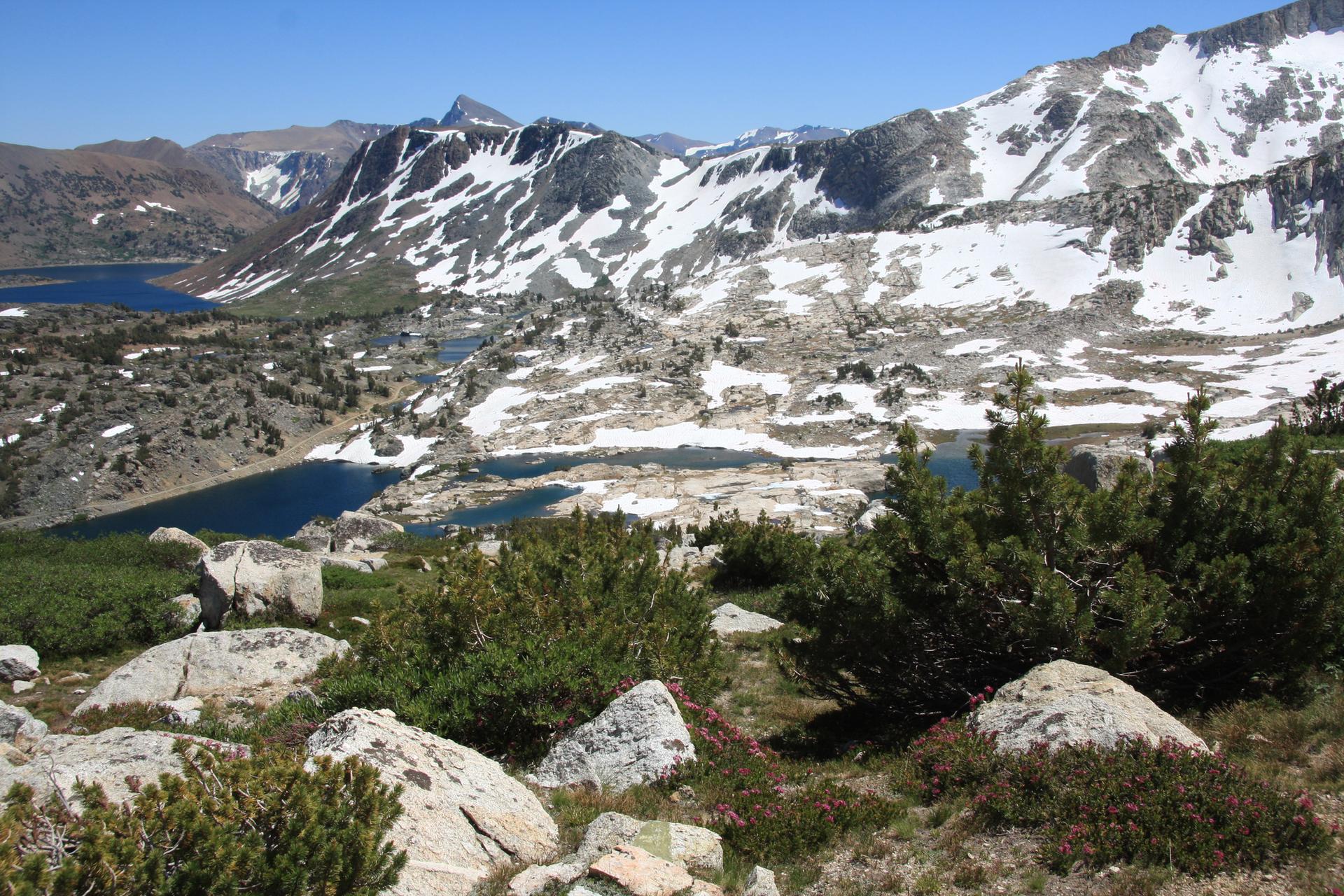 Panoramic view of snow-capped mountains, multiple lakes, and rocky terrain.
