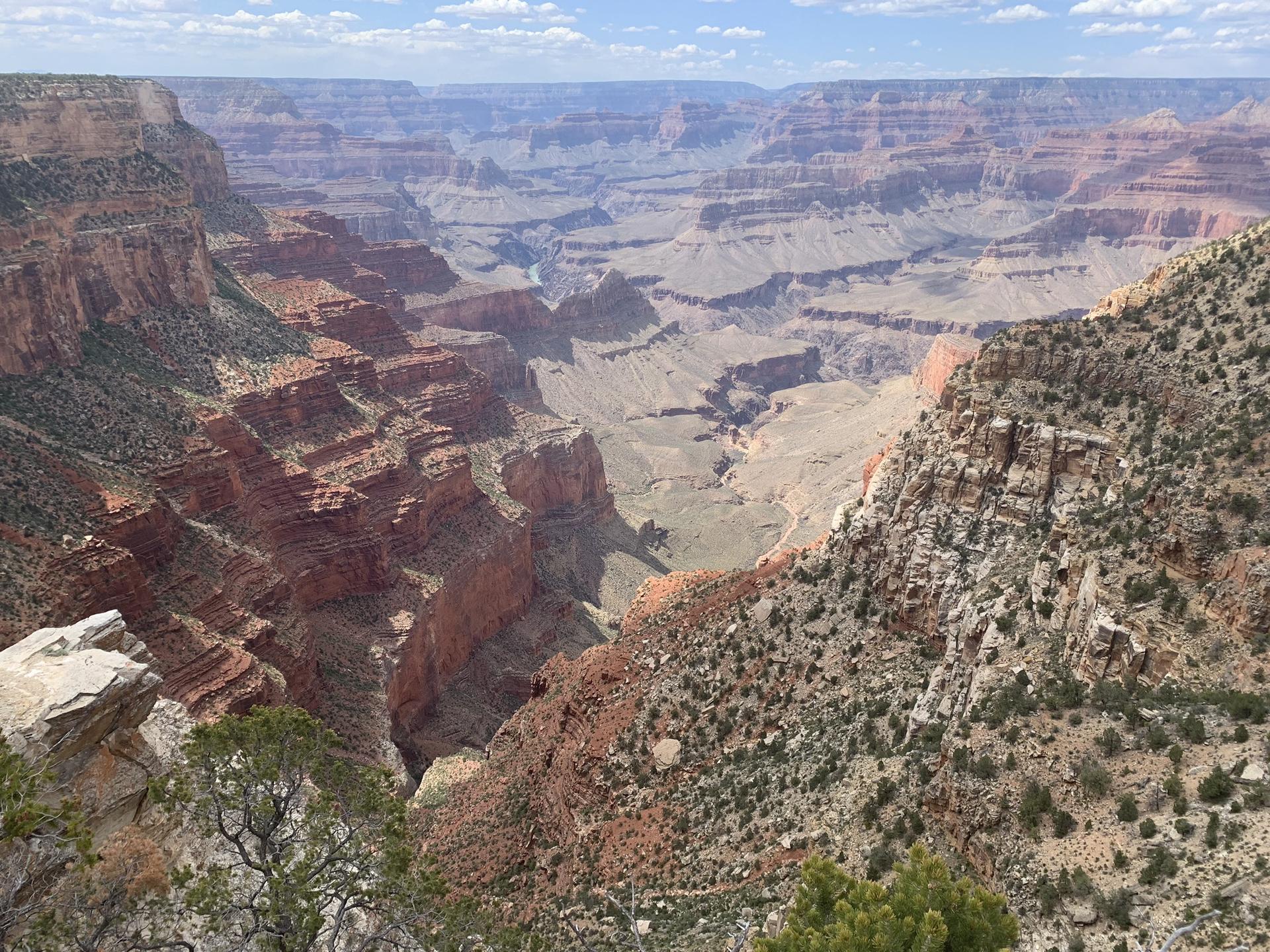 Dramatic view into a deep, wide canyon with colorful layered rock and sparse vegetation.
