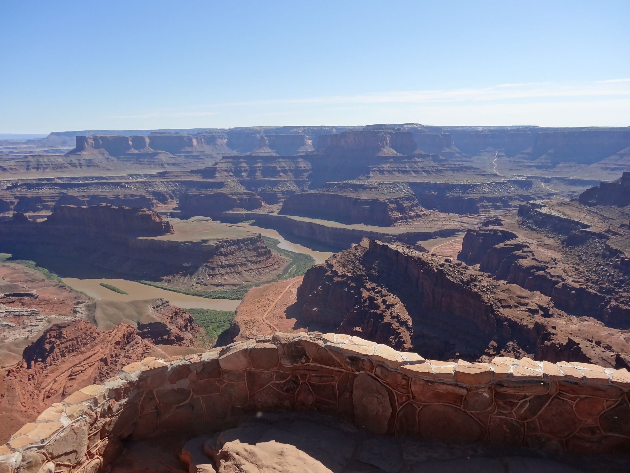 Expansive canyon view with a river, stone wall in foreground, clear sky. - East and West Rim Loop