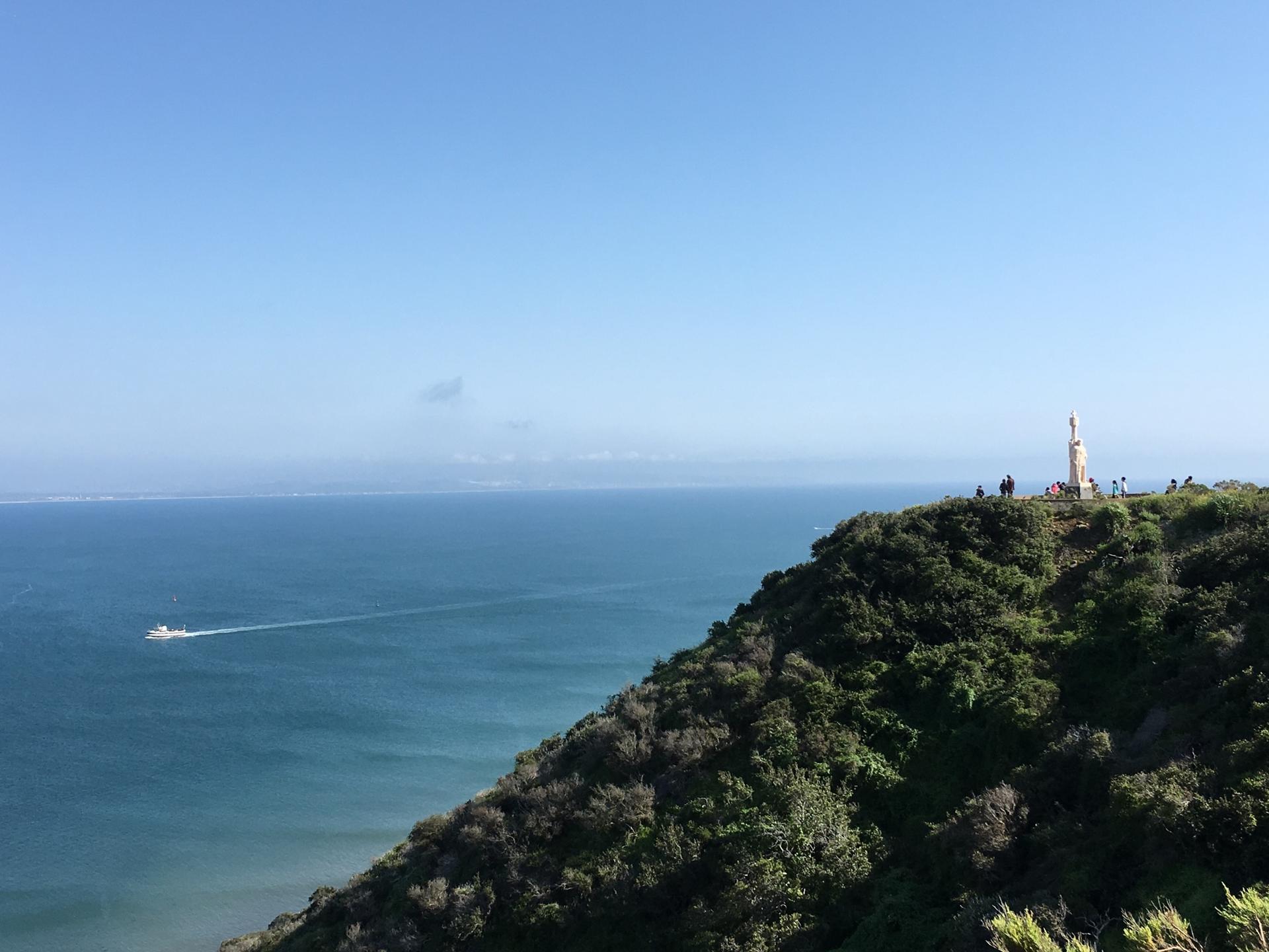 Clear day view of a monument on a green cliff overlooking the ocean.