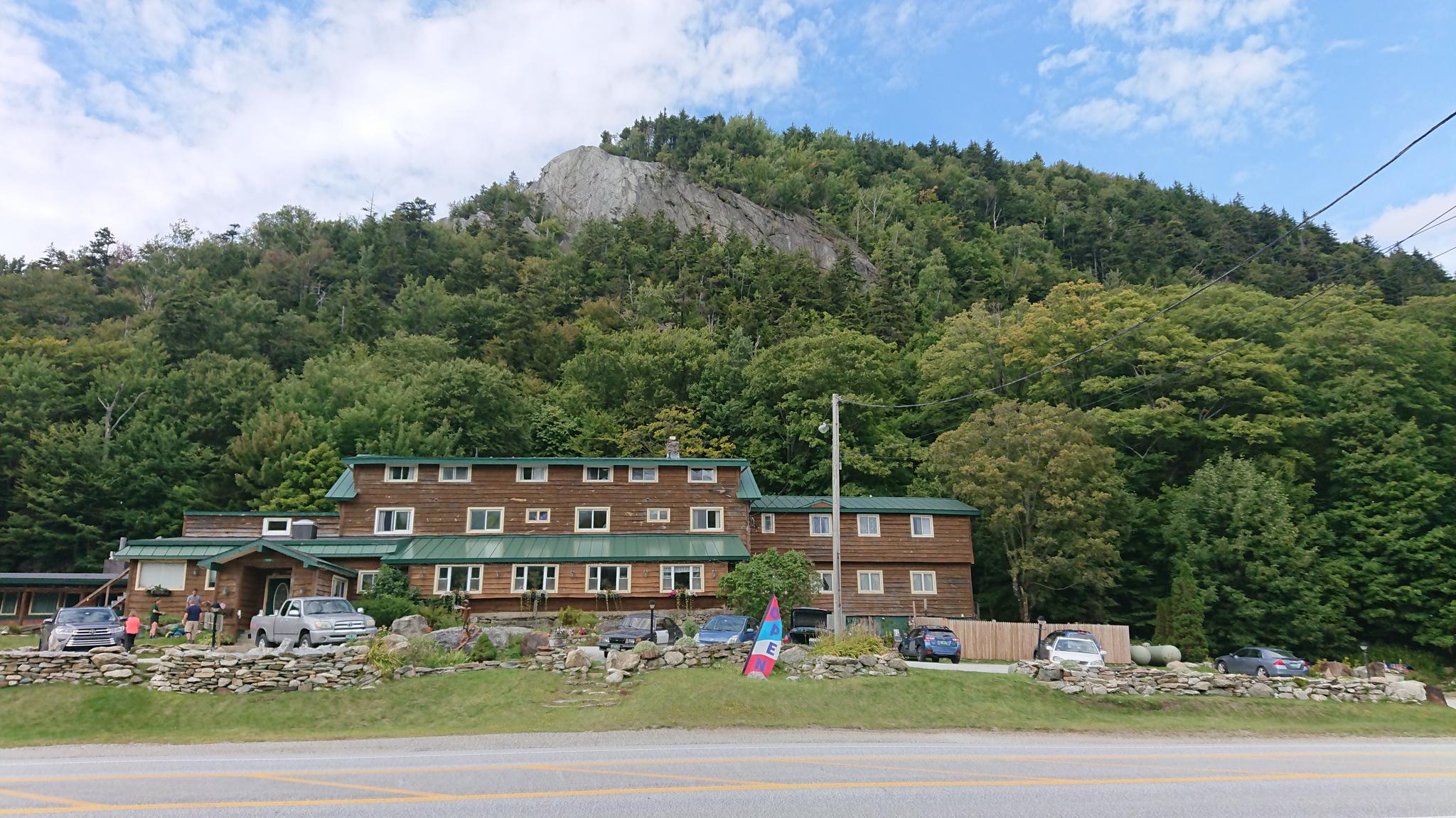 Large wooden building at the base of a forested mountain on a cloudy day.