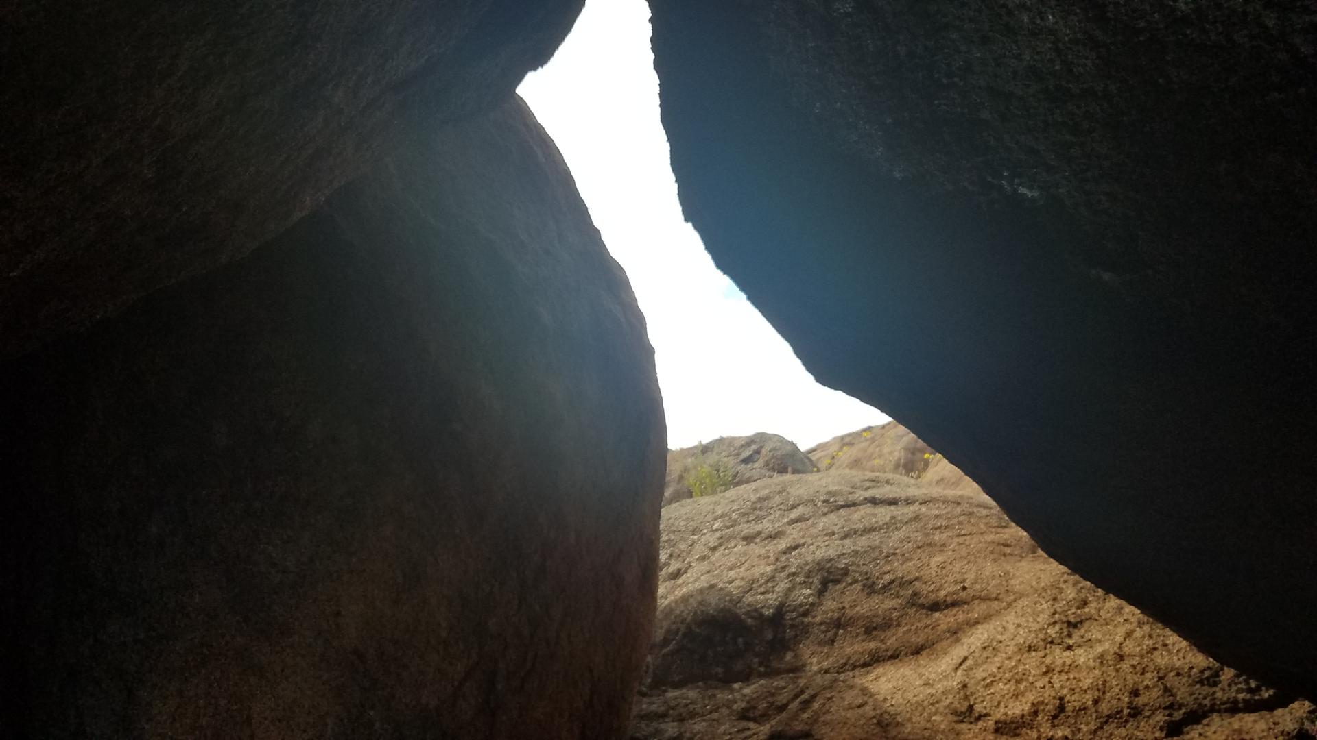 Narrow opening between dark rock formations, revealing a bright sky.